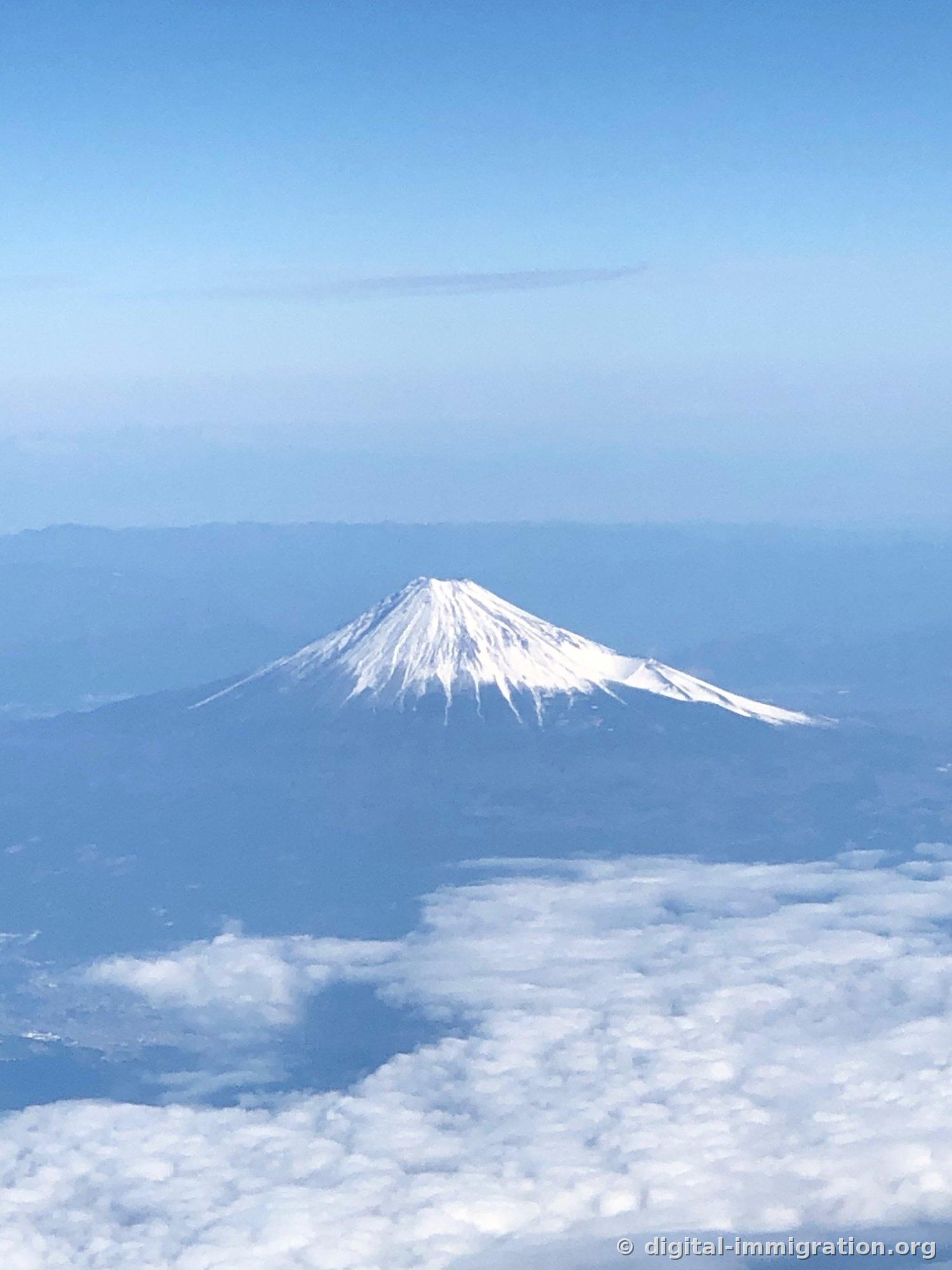 Une vue aérienne du sommet enneigé du Mont-Fuji s'élevant au-dessus d'une mer de nuages, couvert de neige blanche jusqu'aux crêtes des vallées