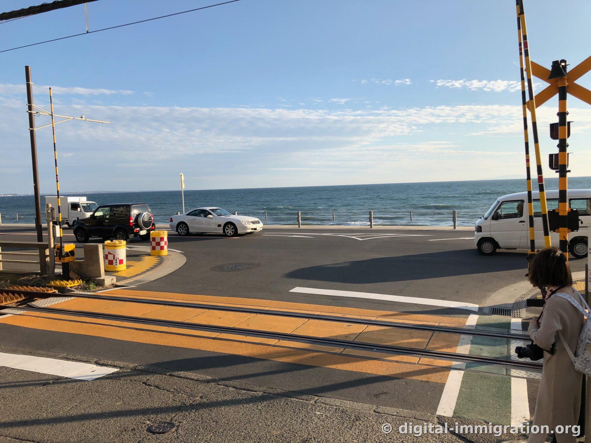 Après le passage du tramway, une personne avec un appareil photo se tient à côté des rails avec la mer et les voitures passantes en vue de l'autre côté de la route, scène d'après-midi
