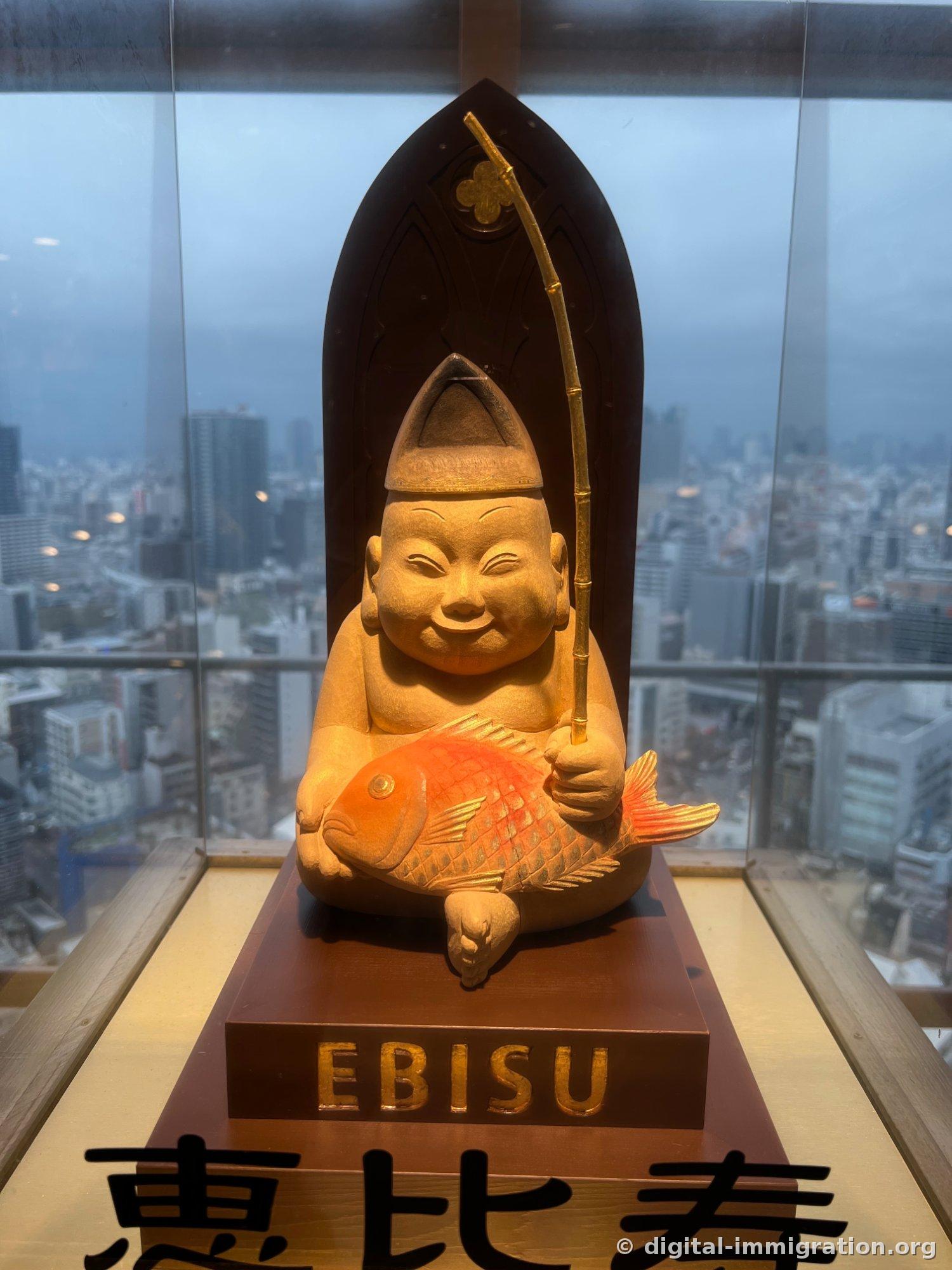 A wooden statue of Ebisu smiling, holding a fishing rod and a red sea bream