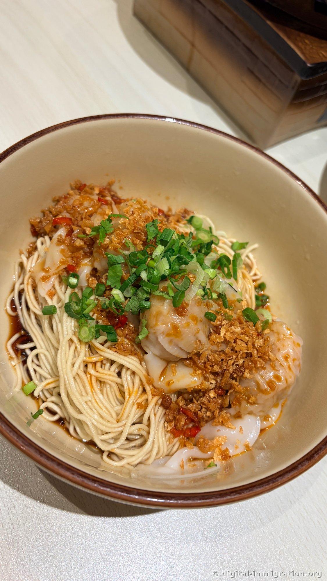 Wonton tossed noodles in a bowl with fine noodles topped with fried garlic and red chili, scallions, and plump wontons