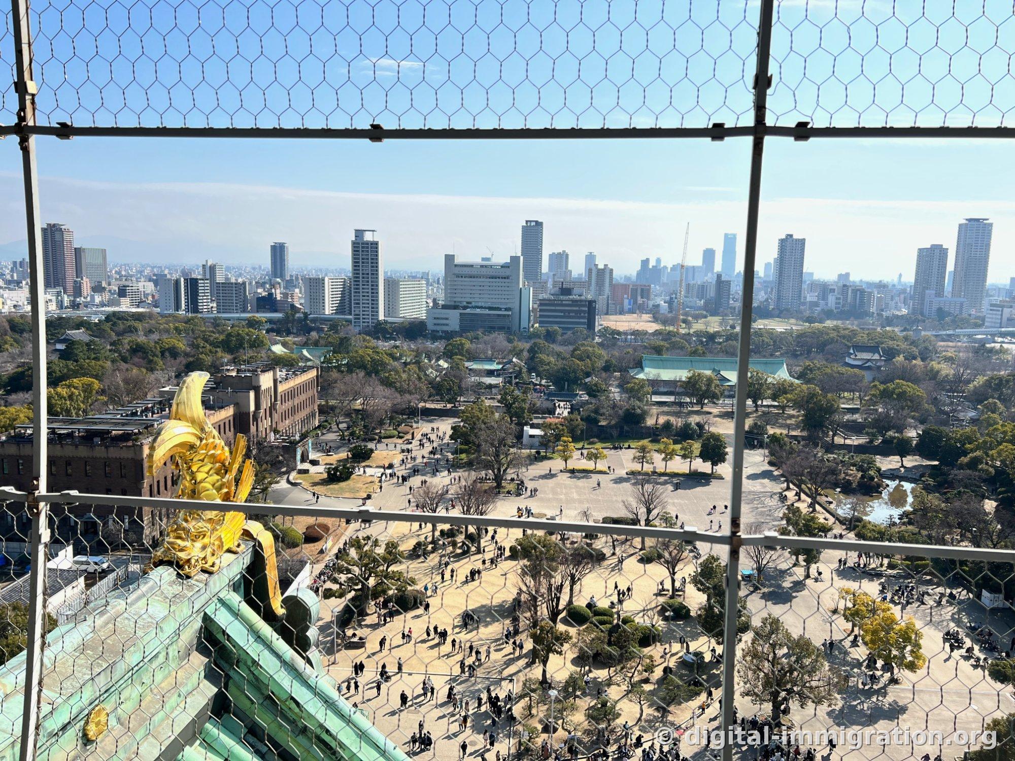 Vue depuis la plate-forme d'observation de la tour de guet au-delà du filet de sécurité de la grande place du château d'Osaka et des gens, la forêt du parc et la ligne d'horizon d'Osaka en arrière-plan