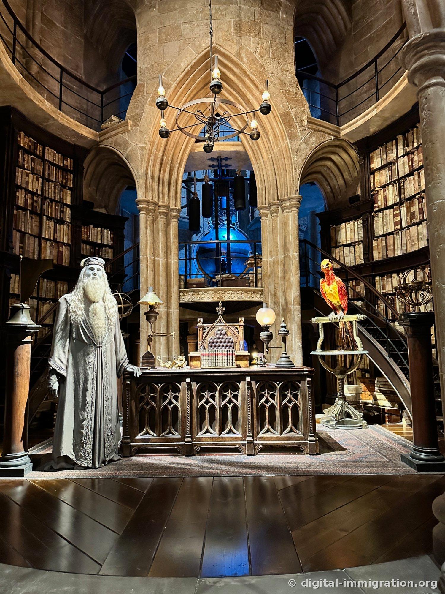 Dumbledore's office set with a figure in silver robes on the left, a red phoenix on a stand to the right, circular bookshelves, and a celestial globe under blue light