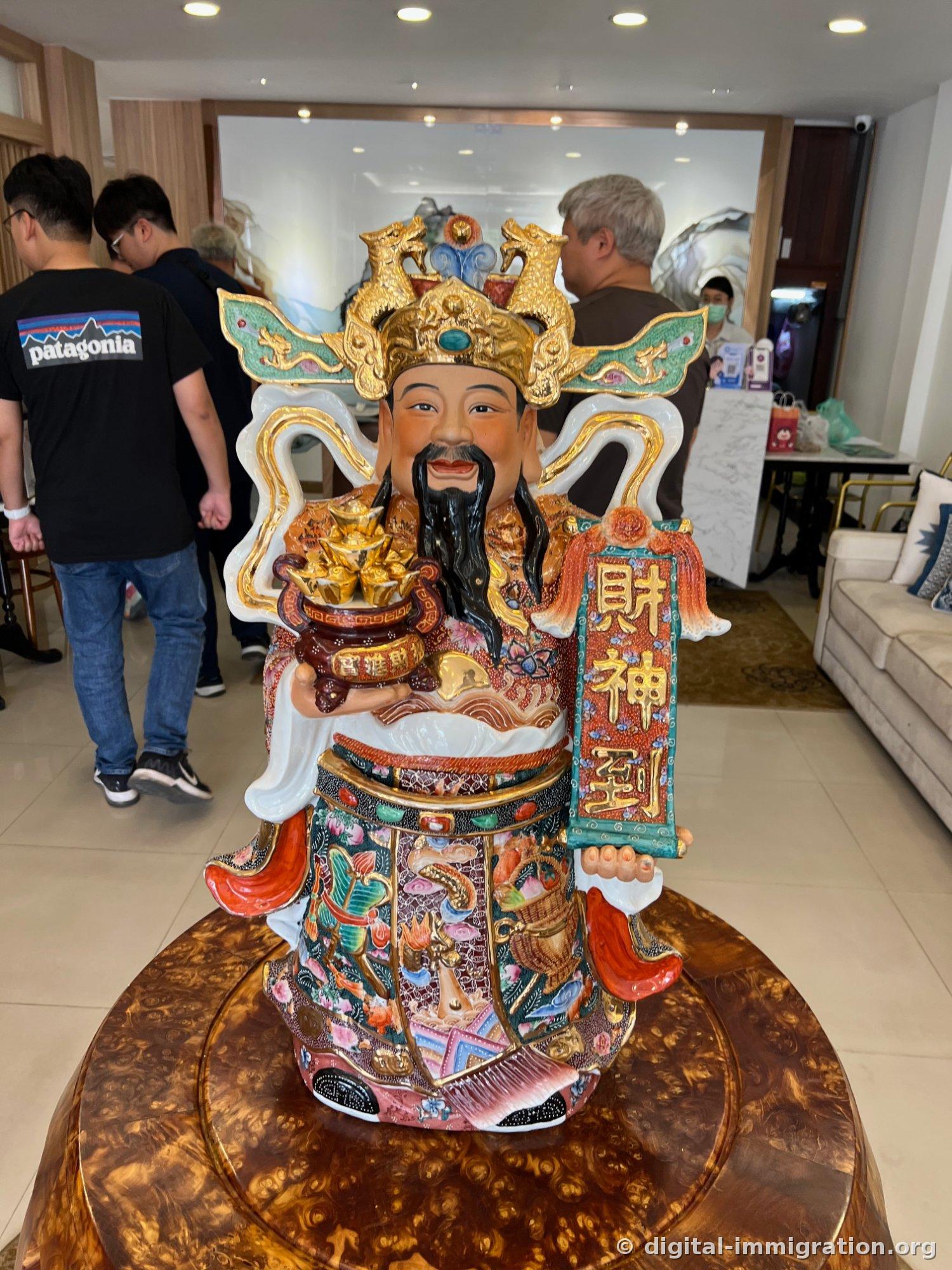 Lobby with an ornate porcelain statue of Caishen, the God of Fortune, sitting on a round table, holding a gold coin jar and a red plaque inscribed with 財神到