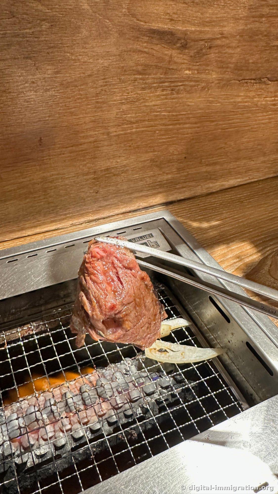 Une bavette épaisse tenue à la pince, dorée en surface avec une teinte brunâtre, avec un morceau d'oignon en dessous sur la grille