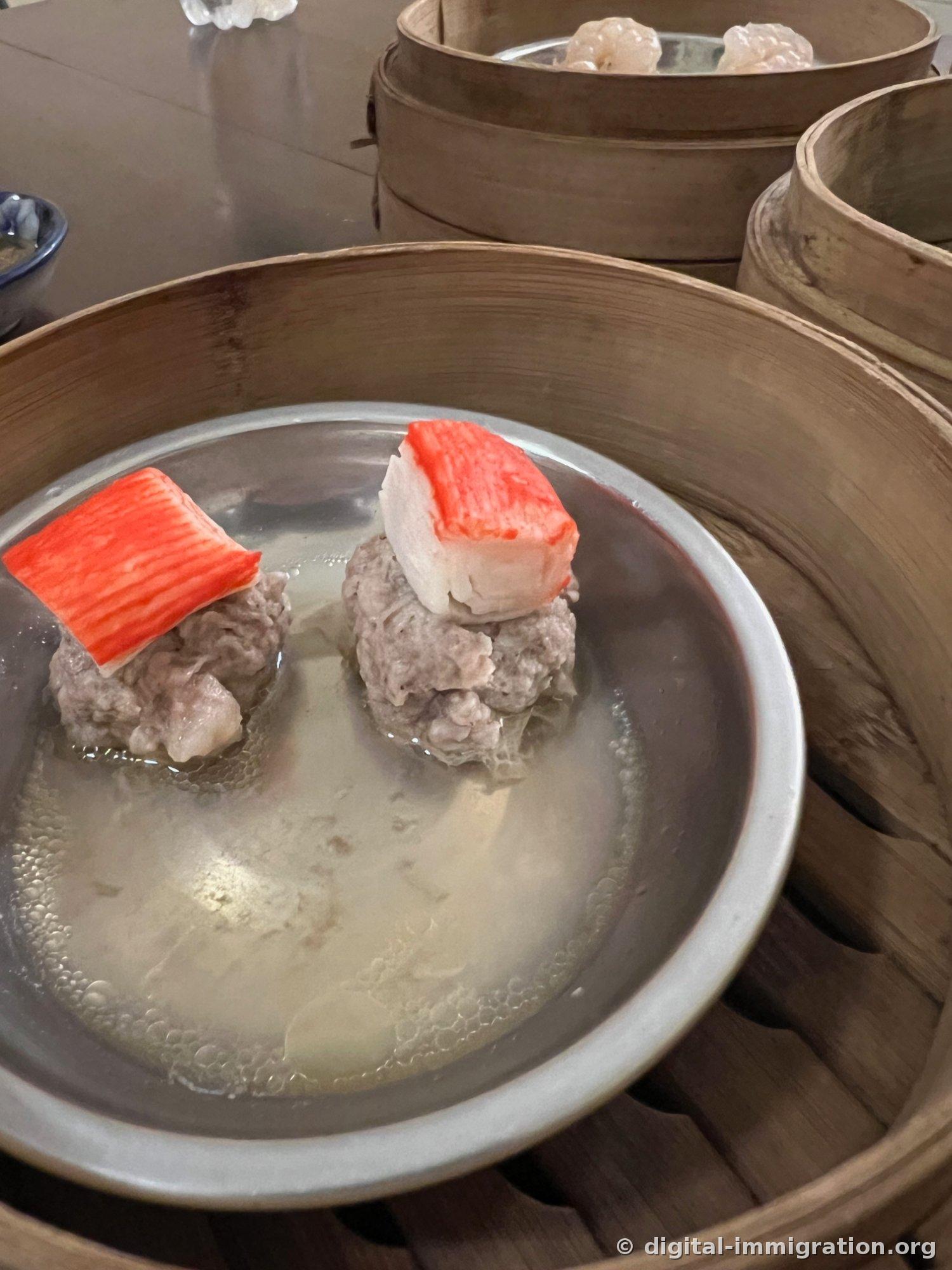 竹のせいろ内の銀色の皿に豚肉団子2個がスープに浸かっており、それぞれの上に赤いカニ身の片が乗せられている