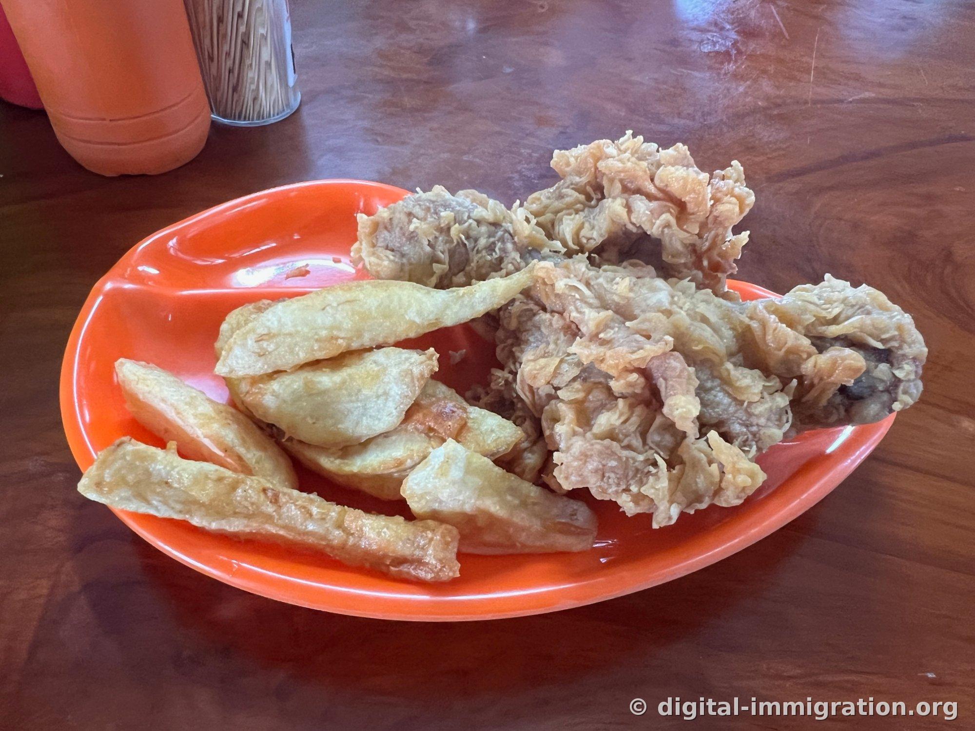 Fried chicken with thin batter and thick-cut fries on an orange plastic plate, with a toothpick holder on a wooden table
