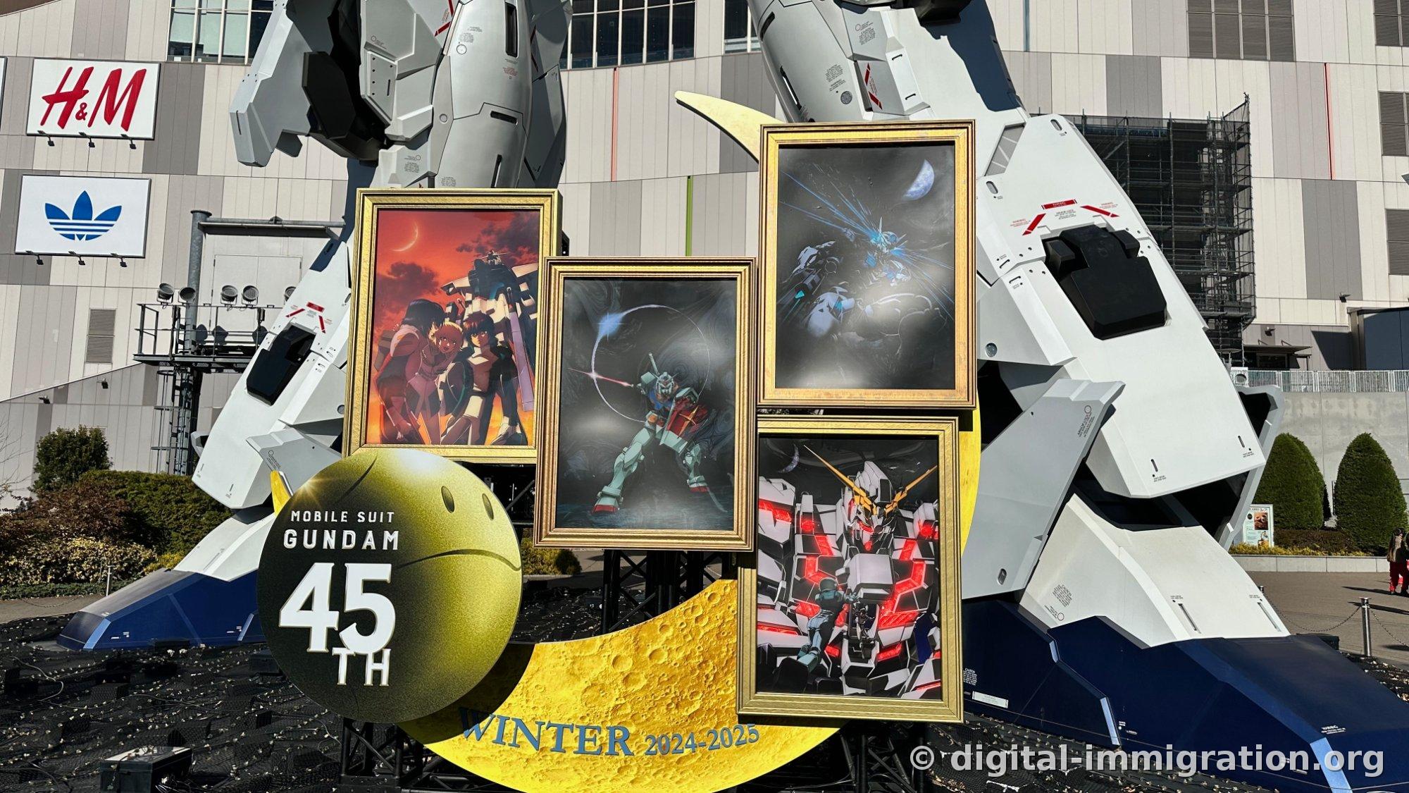 MOBILE SUIT GUNDAM 45TH spheres and yellow crescent moon sculptures installed at the Gundam's base, four Gundam illustrations in gold frames, H&M and Adidas signs on the wall behind