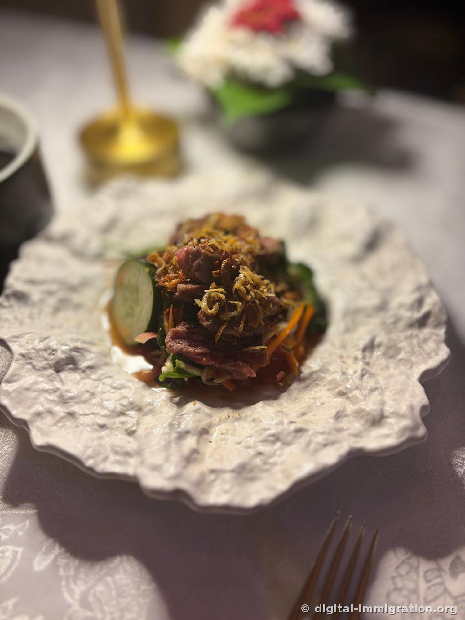Thinly sliced beef with crispy shallots and cucumber and carrot julienne on white ceramic plate