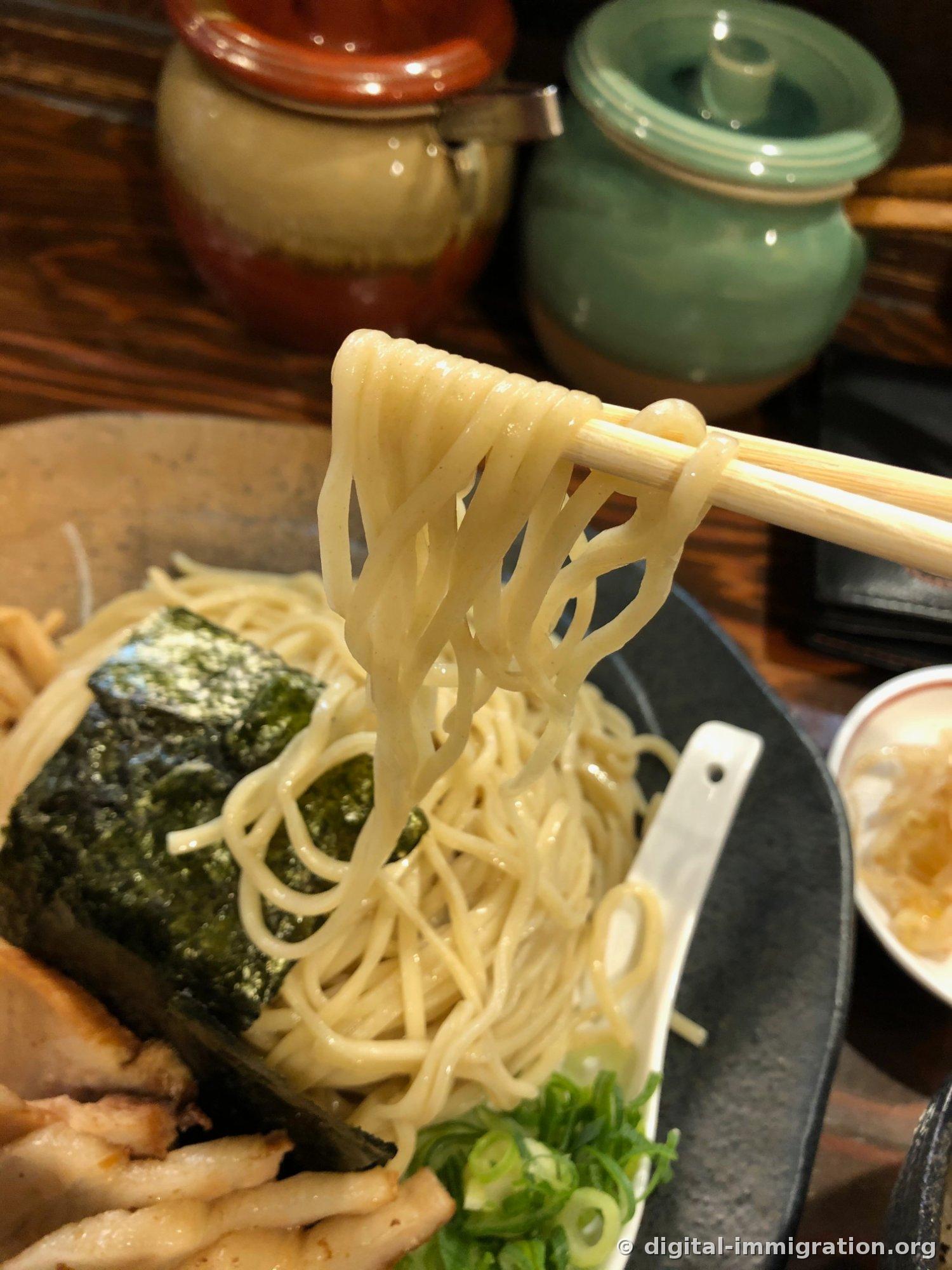 Les nouilles tsukemen fines et droites soulevées avec des baguettes. On voit l'assiette en dessous avec l'algue nori et le char siu