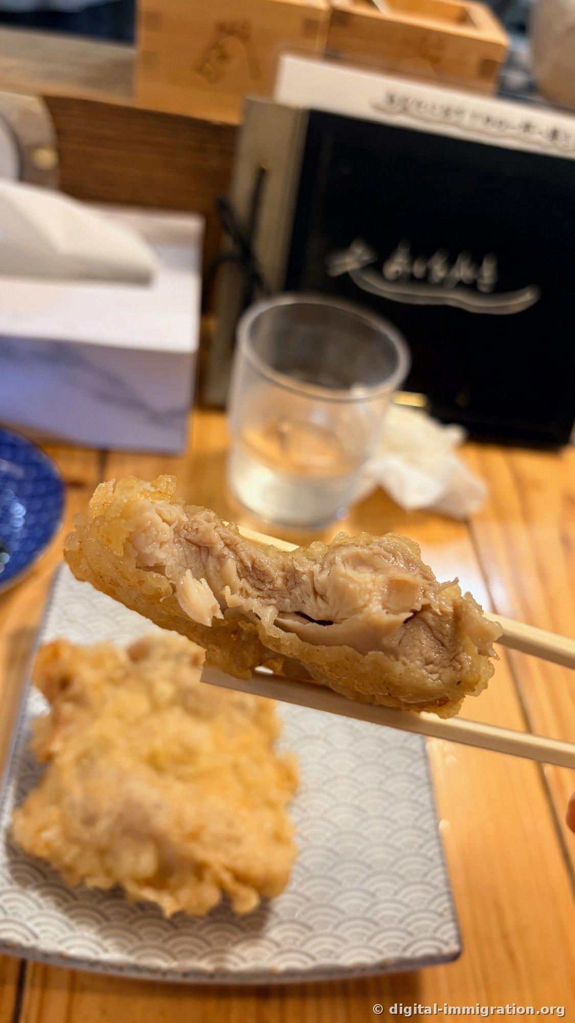 箸で半分に割った鶏天ぷらの断面。白い鶏肉の筋が丸見えで肉汁が光っている