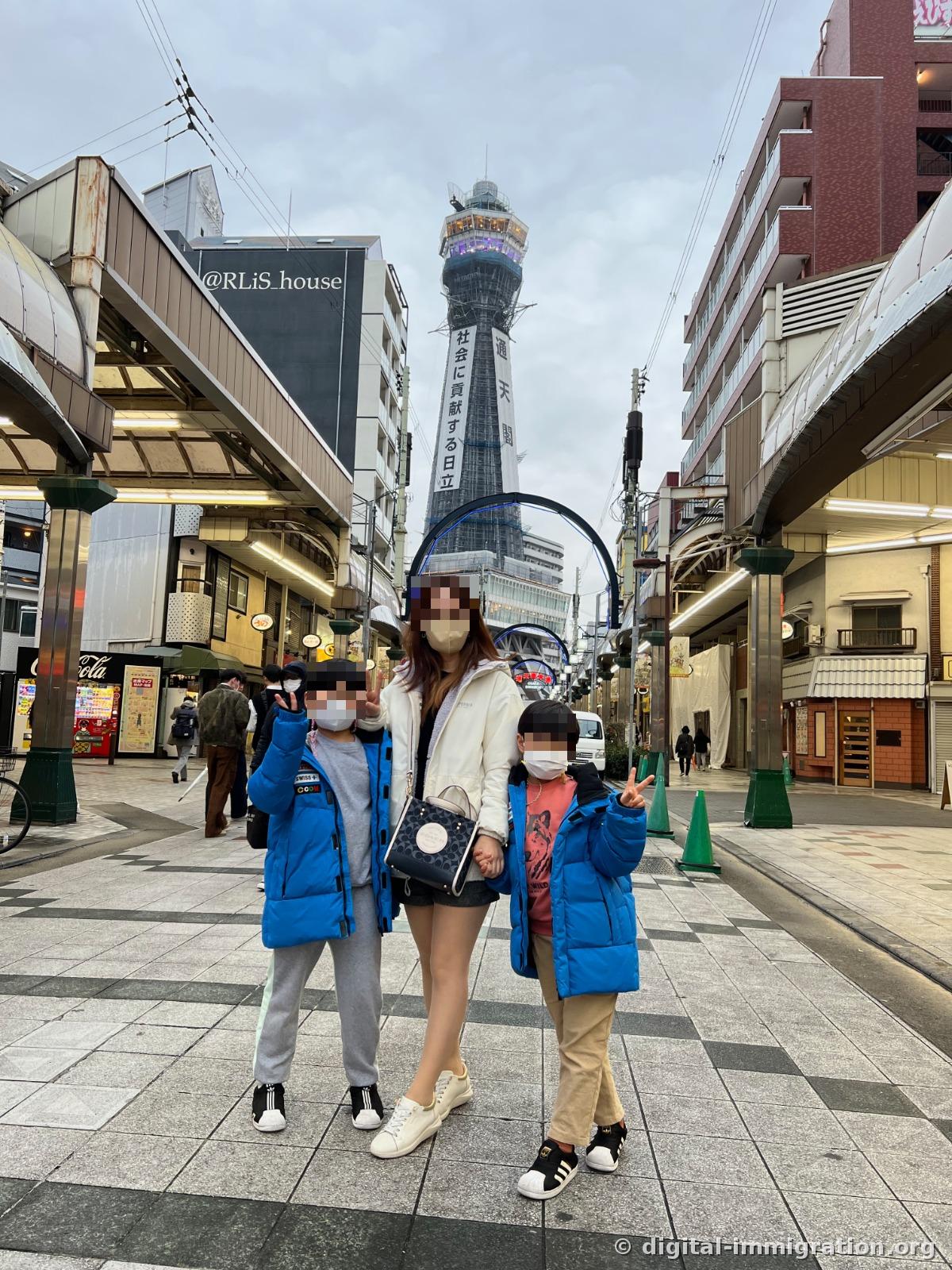 A family standing in the middle of the Shinsekai arcade street with Tsutenkaku Tower in the background
