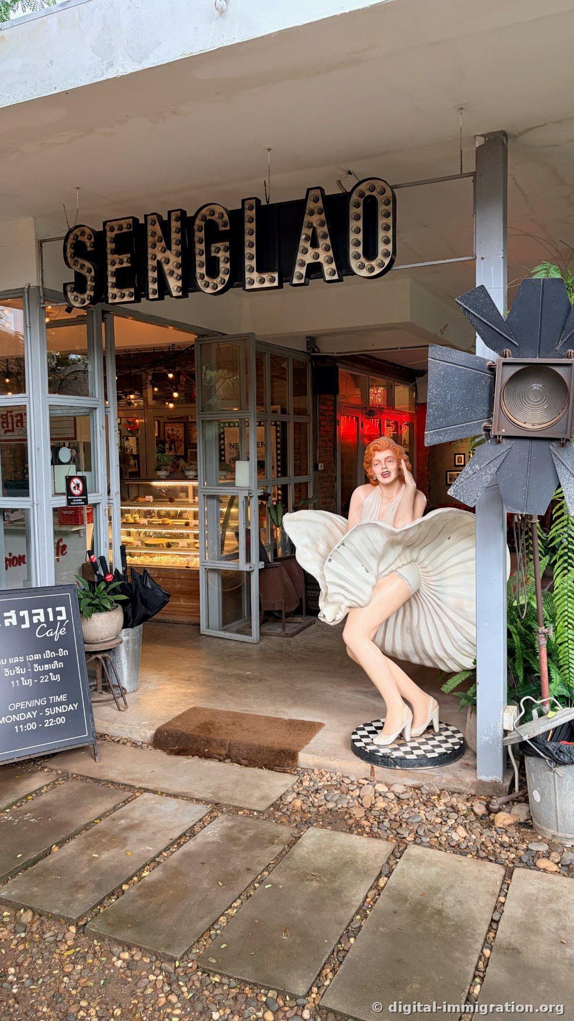 L'enseigne en relief 'SENGLAO' avec des ampoules en dessous, une statue en taille réelle de Marilyn Monroe en robe blanche flottante, et une vitrine de gâteaux visible par la porte vitrée à côté