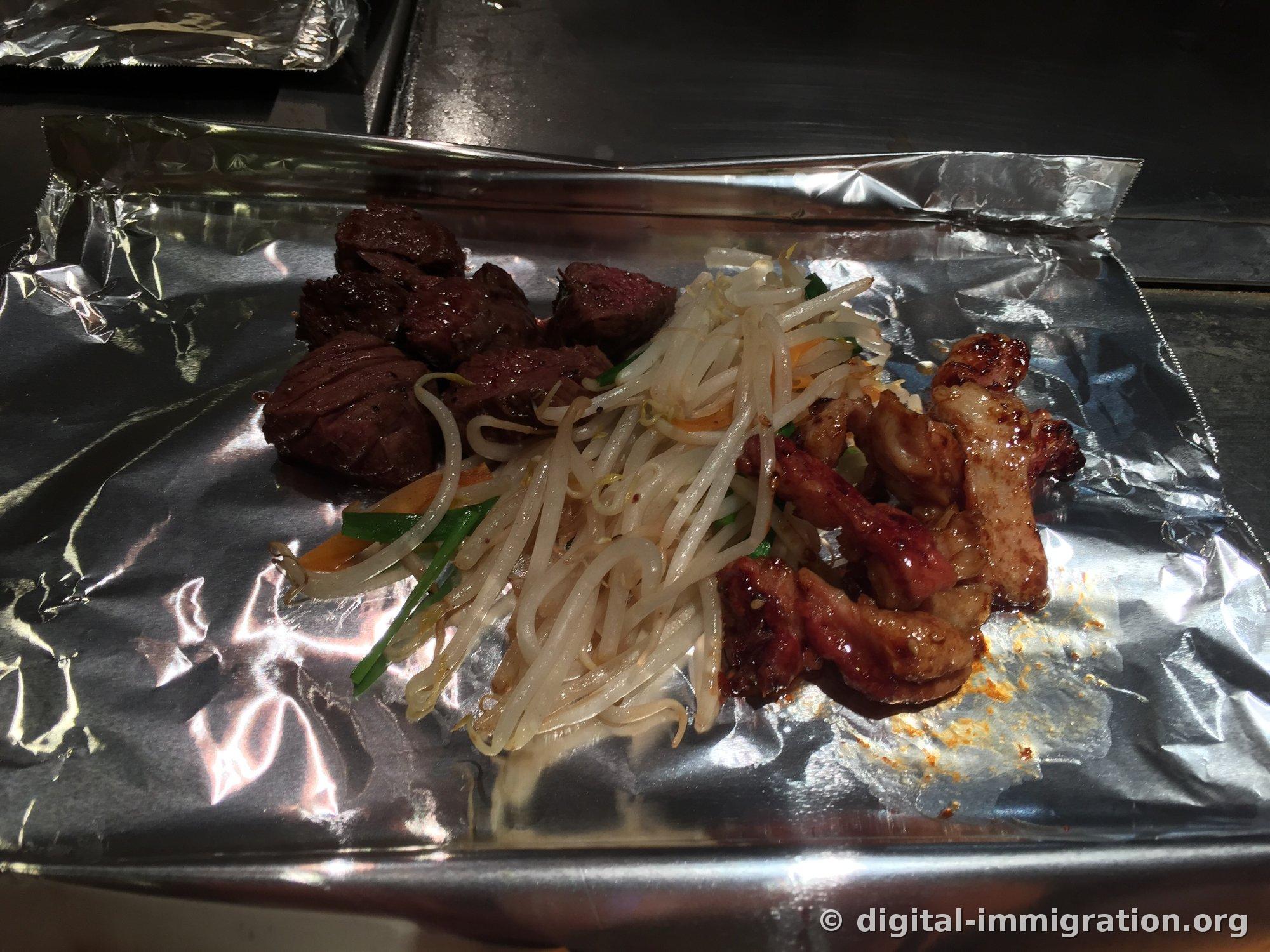 Sur le papier aluminium sur la teppan : à gauche, morceau de boeuf d'un brun foncé grillé, au milieu, sauté de germes de soja et ciboules, à droite, tripes grillées avec sauce brillante