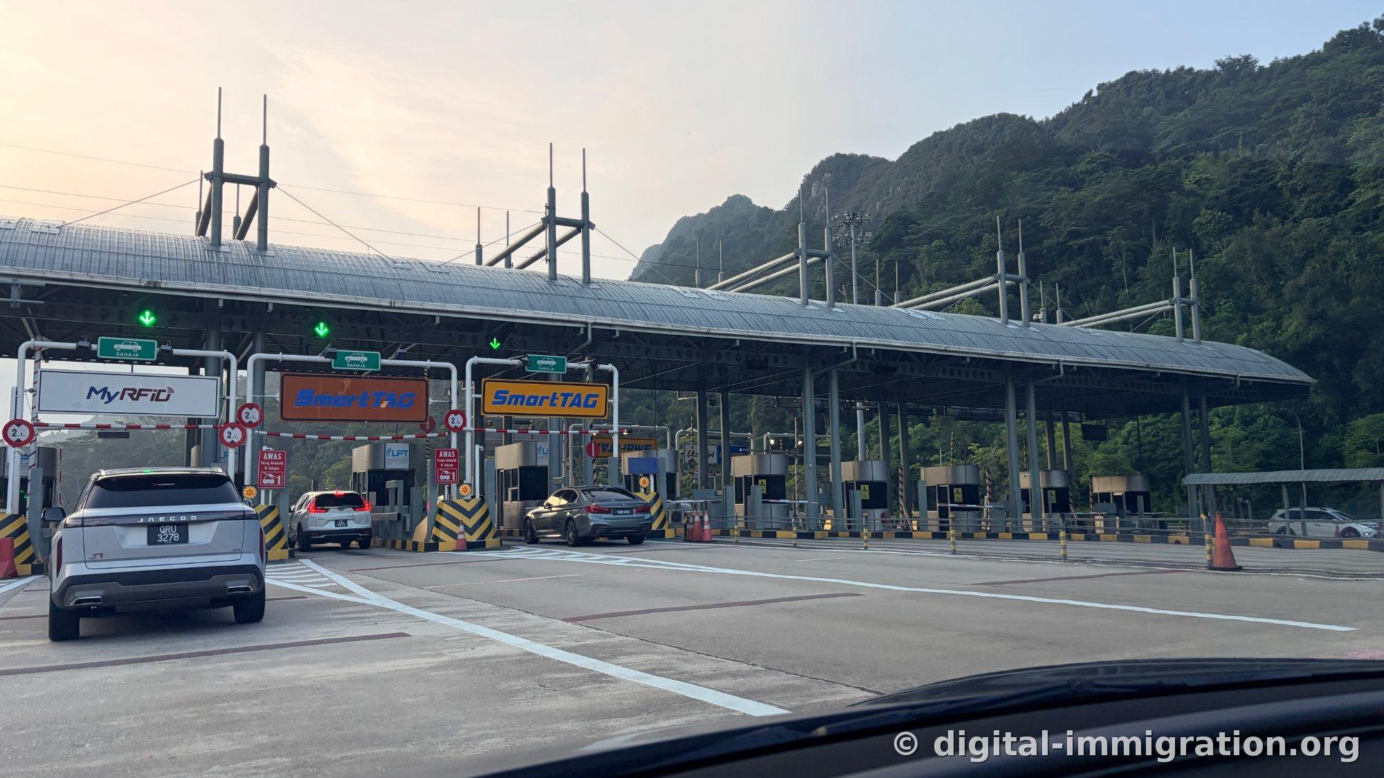 Early morning Malaysian highway toll gate with MyRFID and SmartTAG lane signs visible and green mountains in the background
