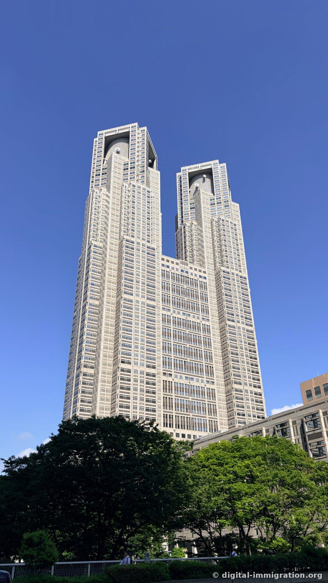 Vue en contre-plongée des deux tours jumelles du bâtiment principal n°1 du bâtiment de l'administration métropolitaine de Tokyo, aux murs de pierre grise, sous un ciel bleu