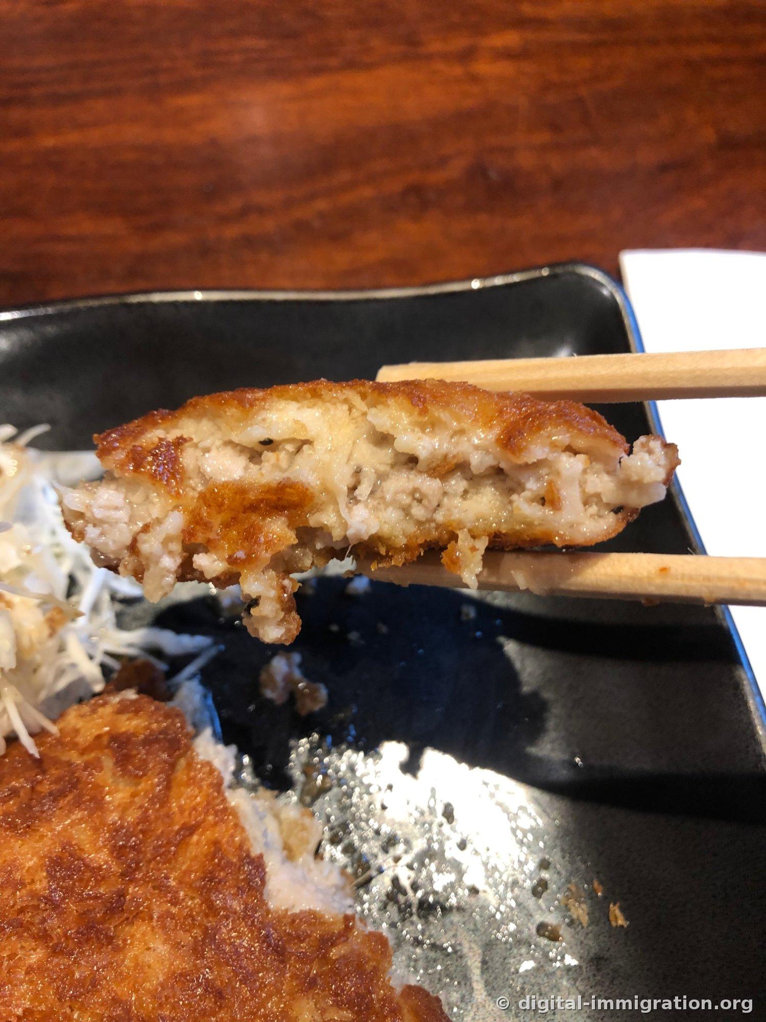 箸で持ち上げたメンチカツの断面。揚げ衣の内側の挽き豚肉が白く、粒が粗く見える