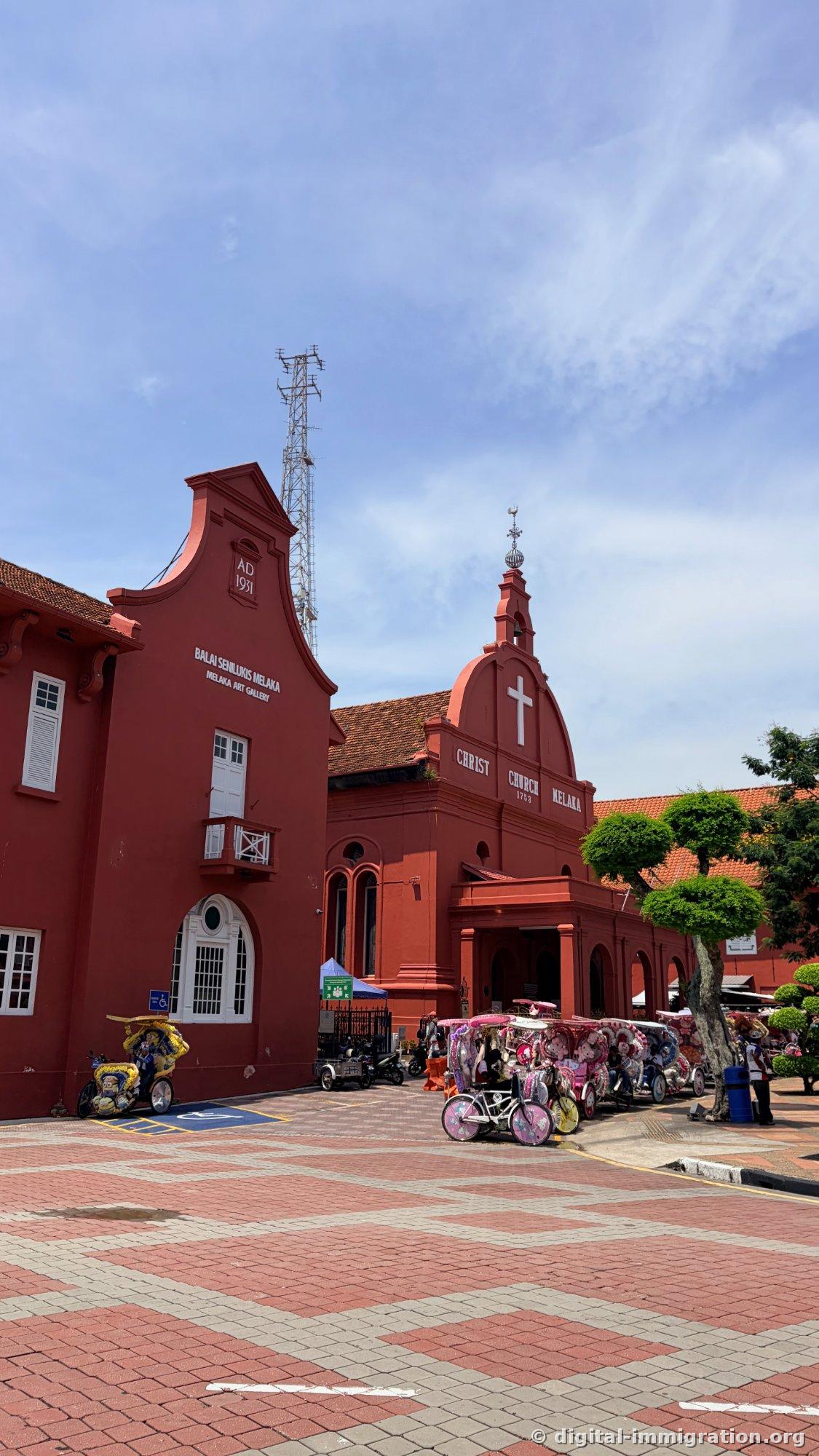 The front of the red Christ Church Melaka and the Melaka Art Gallery building marked 'AD 1931' to its left. Character-decorated trishaws line up in the square in front