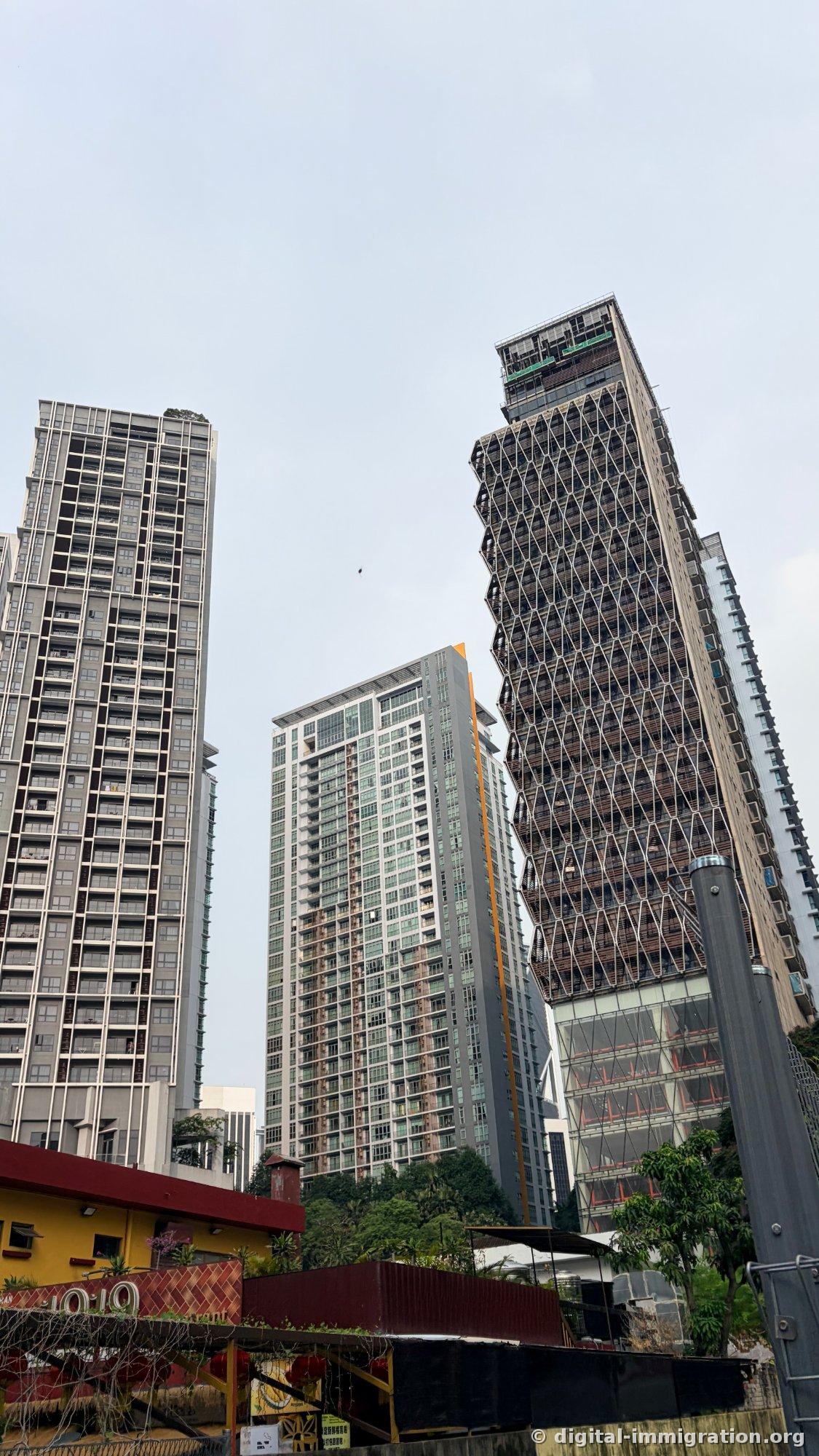 An overview showing the single-story yellow building with '1919' painted on its red-roofed facade, nestled beneath three residential condos and a diamond-lattice tower