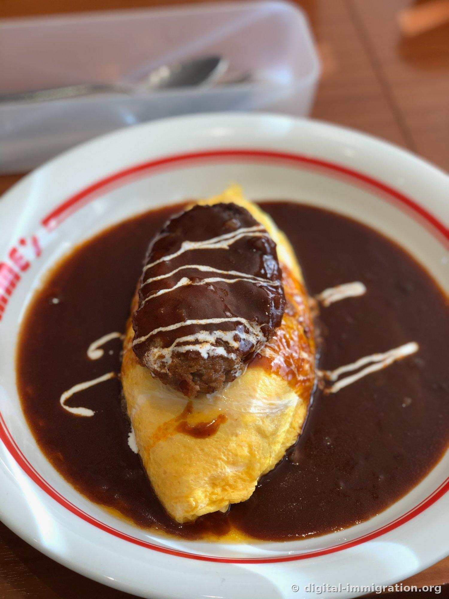 Gros plan de l'omurice. La surface jaune brillante de l'œuf et le steak haché dessus, avec des traits blancs de crème, sont clairement visibles