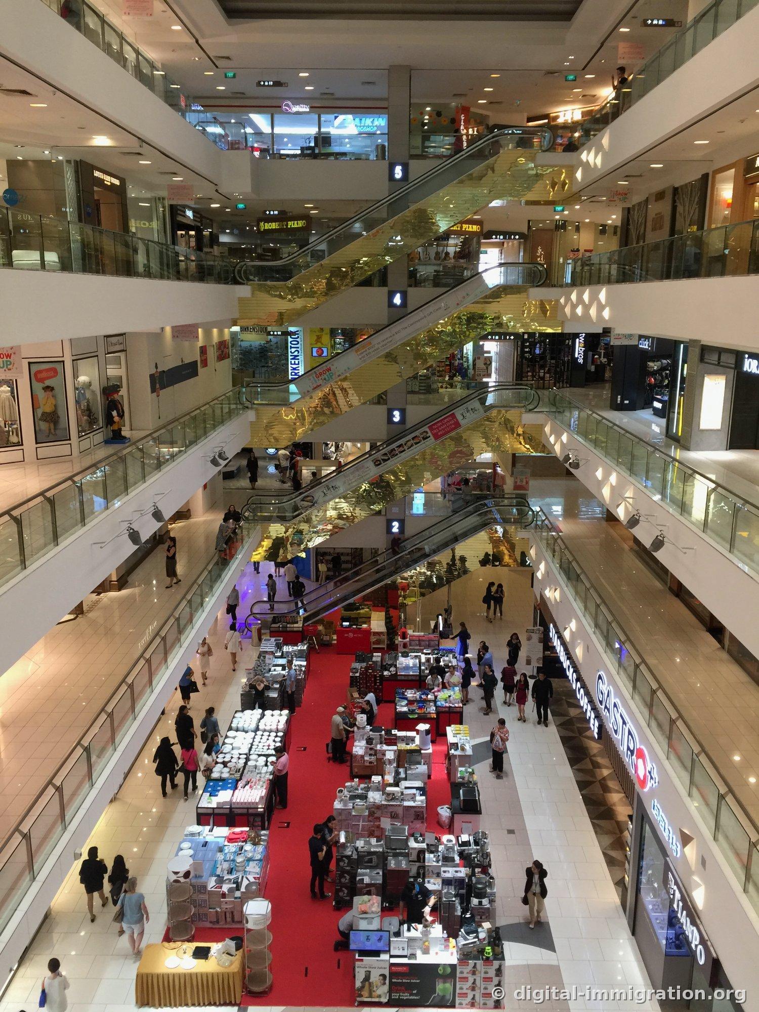 Vue de l'atrium du Centrepoint depuis l'étage supérieur. Les escaliers roulants dorés traversent en diagonale et un étal de soldes d'appareils électroménagers s'étend sur le tapis rouge du premier étage