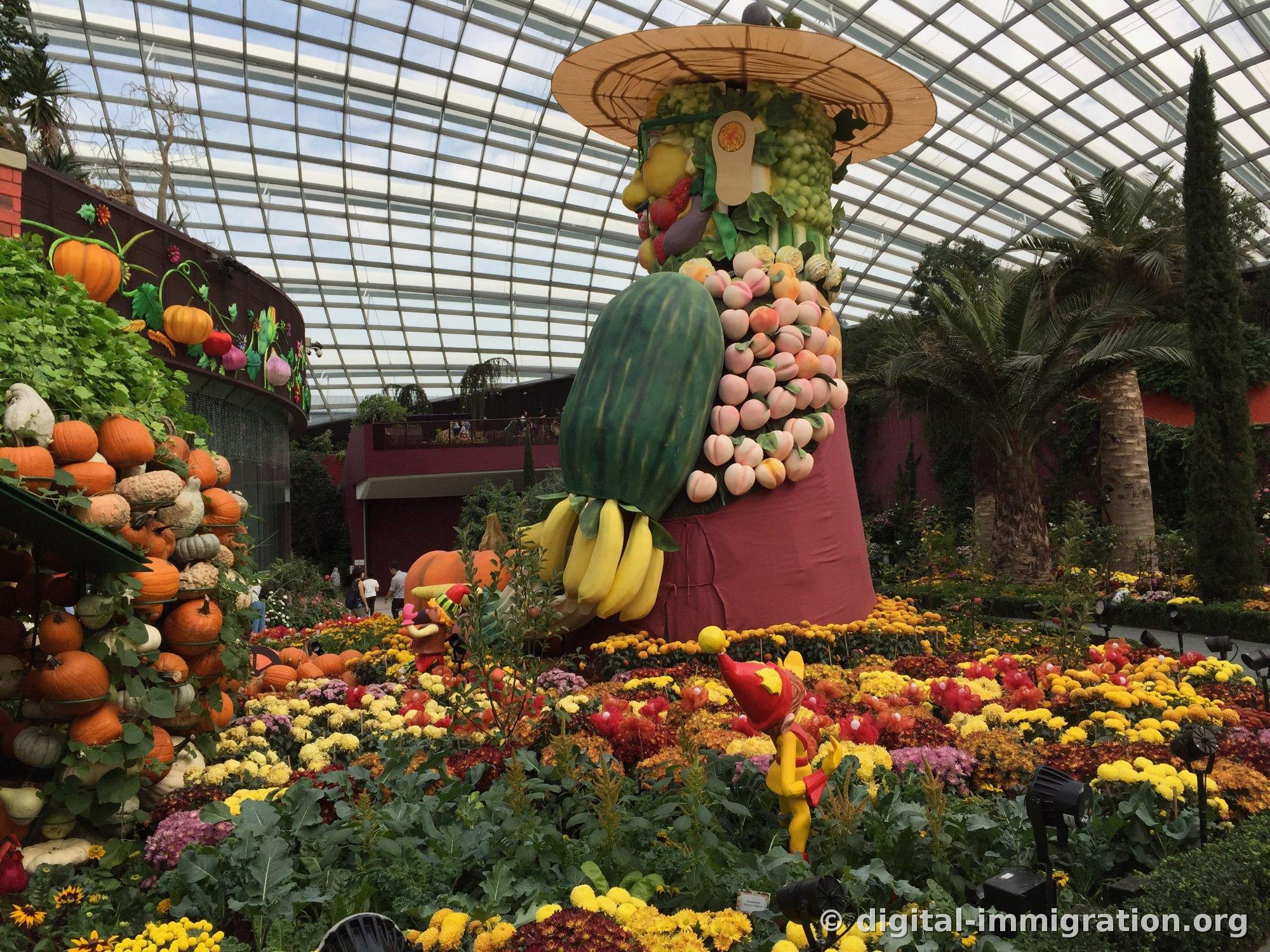 A giant figure made of fruit and vegetables viewed from the side, with peaches and grapes stacked in layers and a pumpkin wall stacked on the left