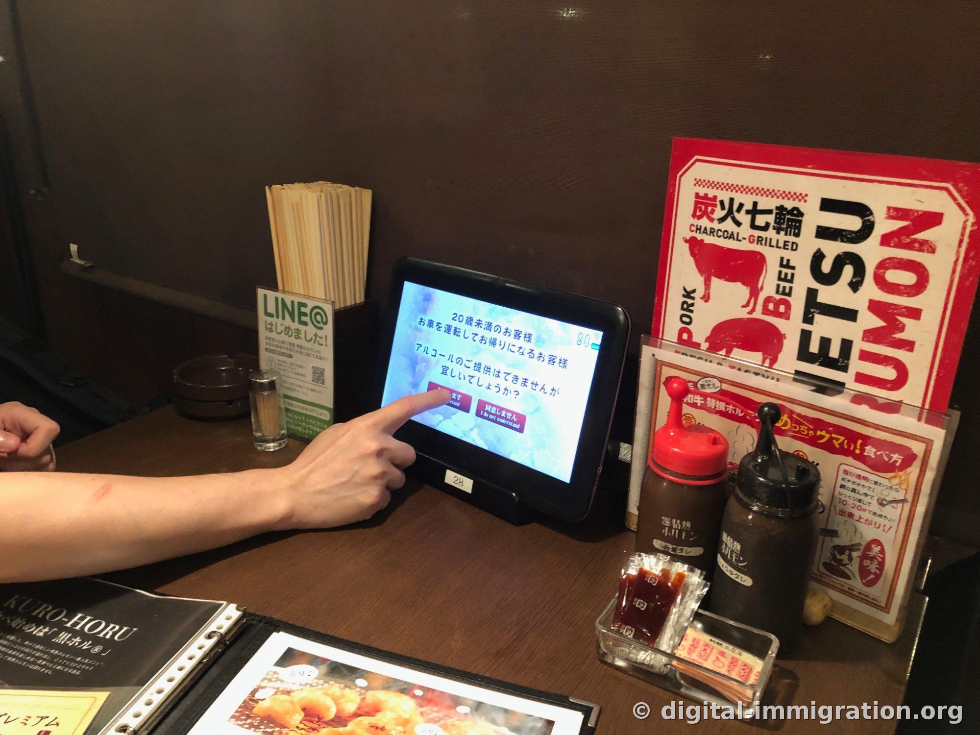 Un doigt appuyant sur l'écran de vérification d'âge sur la tablette et les pots d'assaisonnement et porte-baguettes sur la table