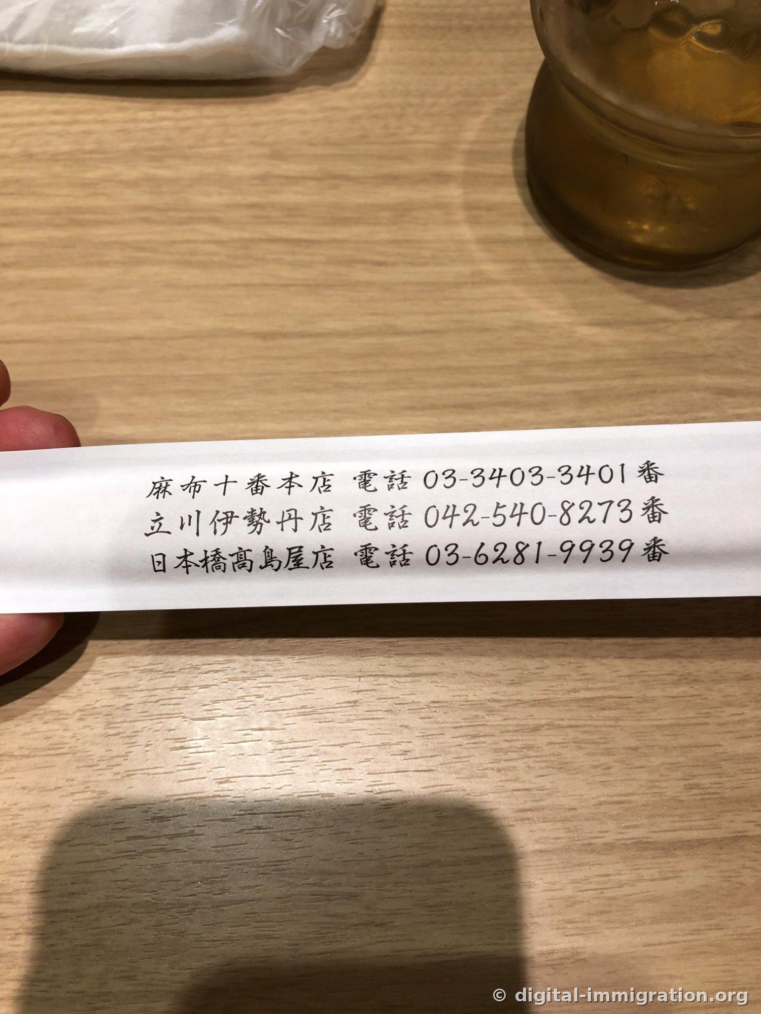 Back of the chopstick wrapper with phone numbers for Azabu-Juban main branch, Tachikawa Isetan branch, and Nihonbashi Takashimaya branch printed