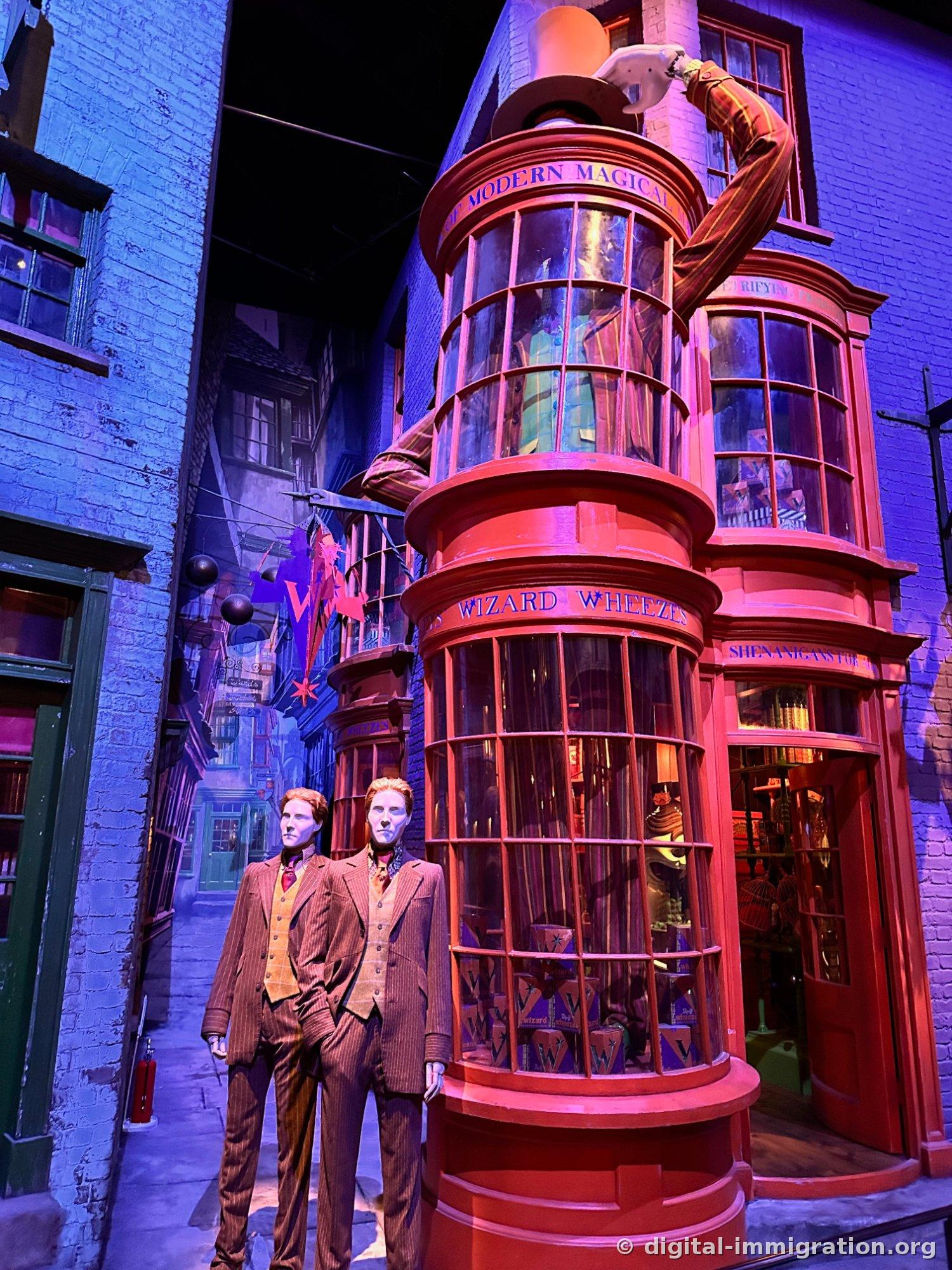 A red-painted Weasleys' Joke Shop storefront with Fred and George mannequins in front, and an animated figure on the roof tipping a hat