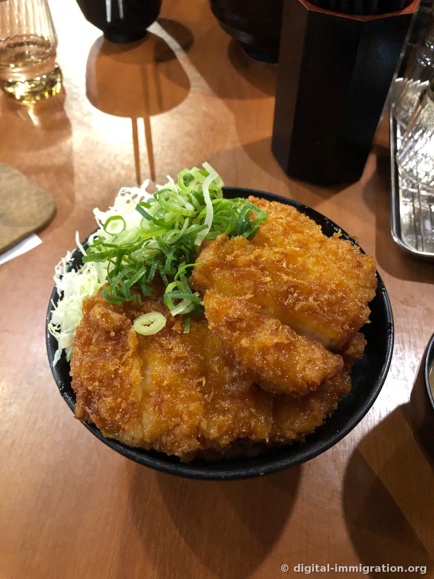 Katsu don avec sauce dans un bol noir, avec ciboule finement hachée et chou finement tranché sur le riz frit brun foncé