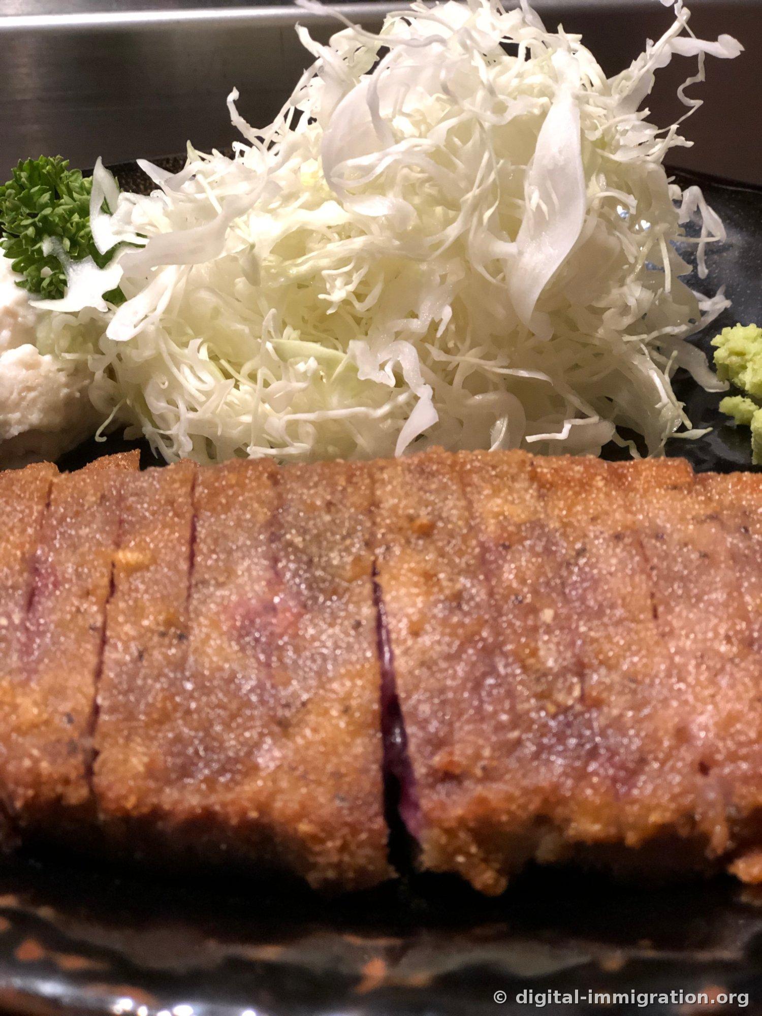 Gros plan de la panure de Gyukatsu. Côtelette de bœuf avec fine panure, tranche montrant l'intérieur encore cru, avec chou émincé abondant, persil et wasabi empilés derrière