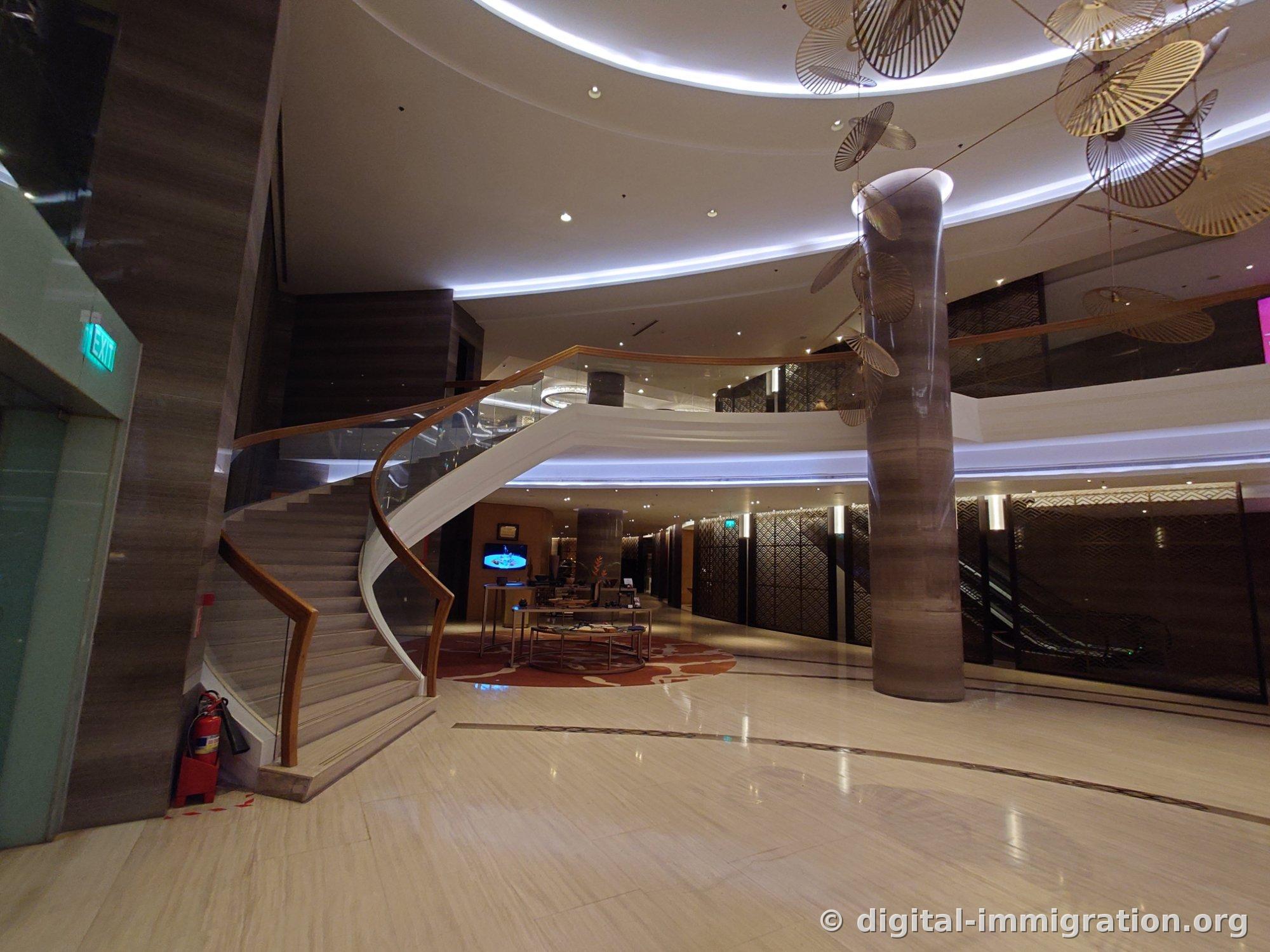 Curved staircase with glass railing and wooden handrail, first floor with red carpet and display table on the side