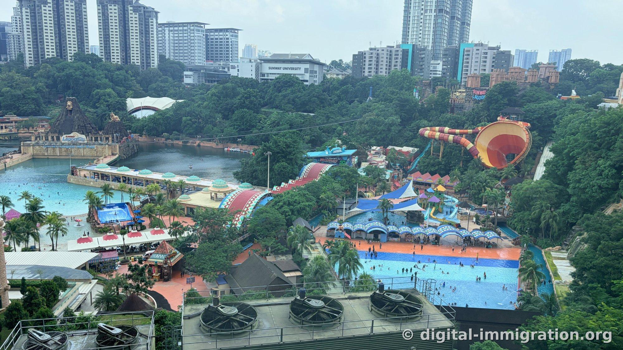 从高处俯瞰 Sunway Lagoon 全景，造浪池和红色漏斗形水滑梯，背后的 SUNWAY UNIVERSITY 建筑