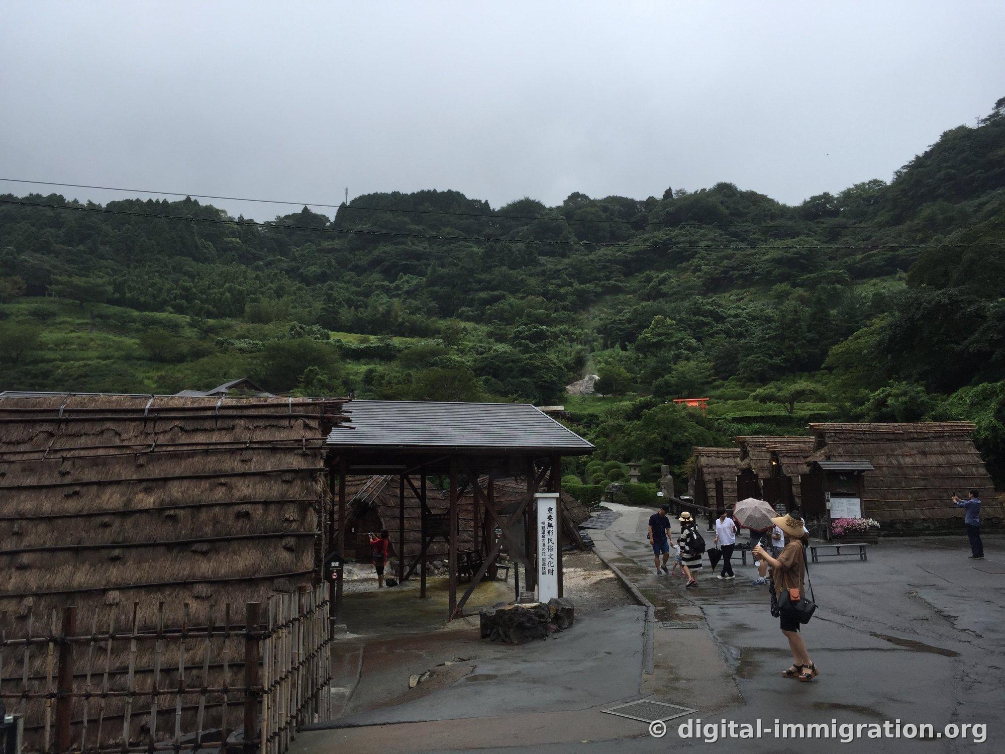 Des petites cabanes de fabrication de yunohana au toit de chaume alignées sur une pente avec une colonne d'affichage lisant '重要無形民俗文化財' à Myouban Onsen