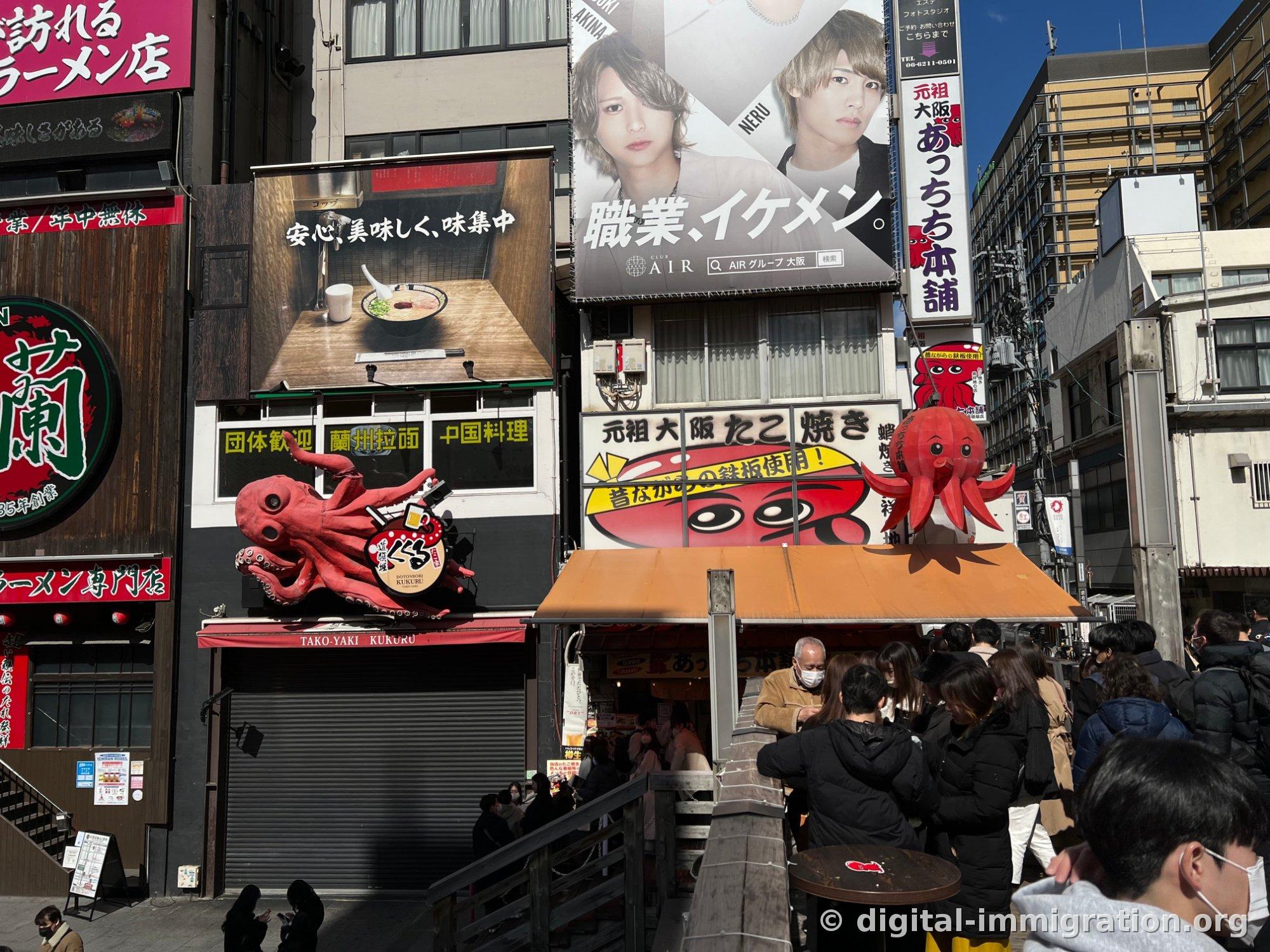 Énorme statue de poulpe rouge du takoyaki Kukuru et l'enseigne Atchichikonpo à côté, avec une file d'attente devant