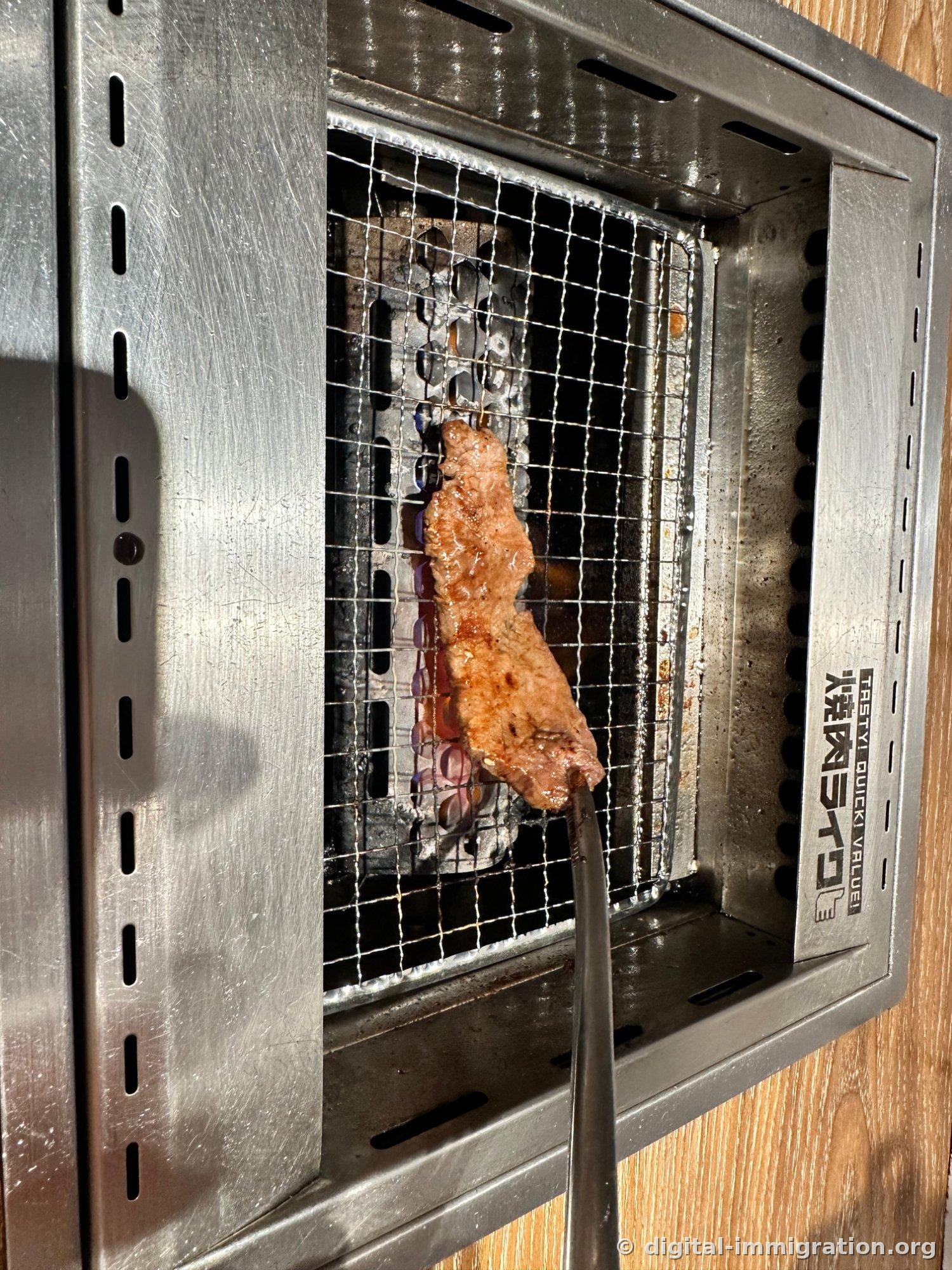 Sur la grille du petit foyer en acier inoxydable pour une personne, un morceau de viande finement tranchée dore à la chaleur