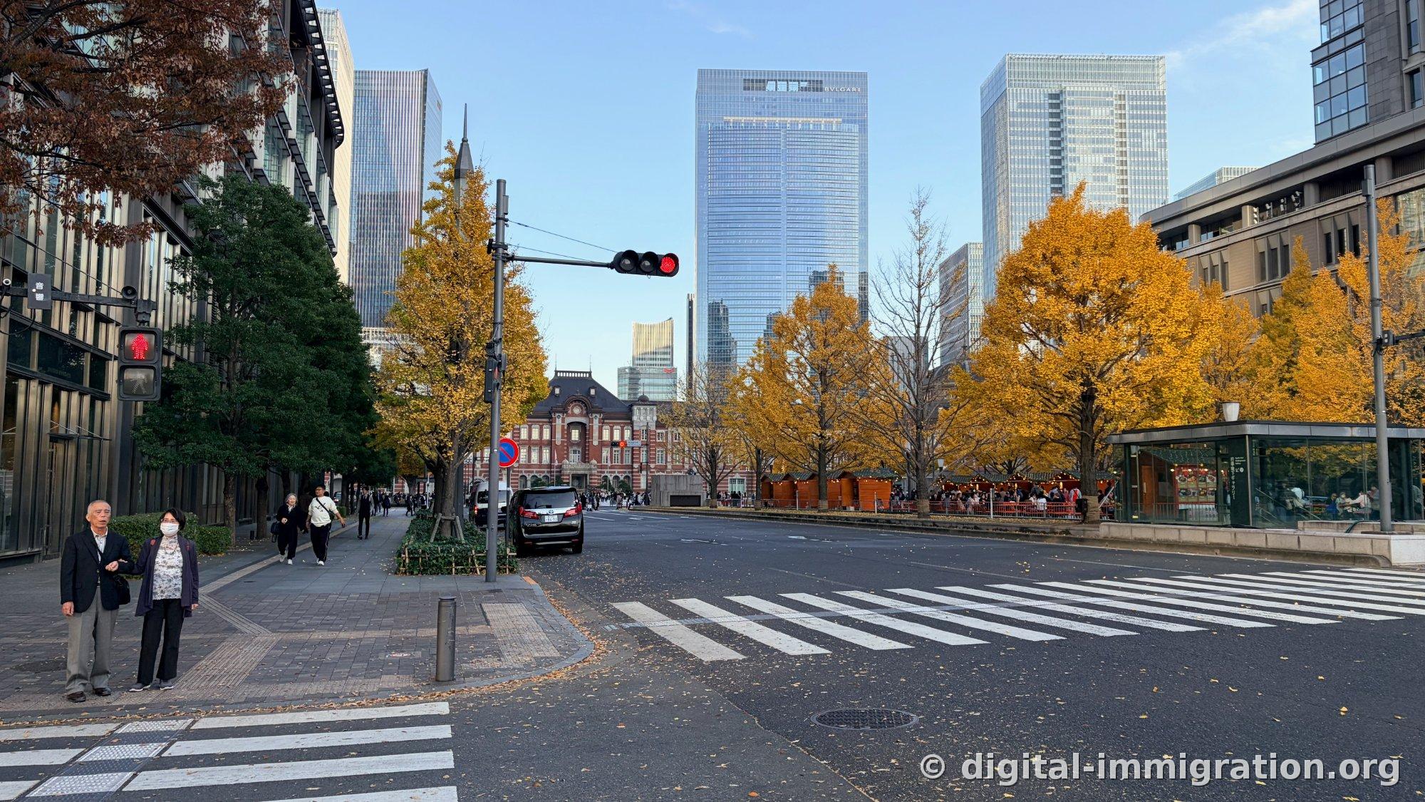 Au-delà du passage pour piétons avec le feu rouge allumé, les ginkgos jaunes et les chalets du marché de Noël, avec le bâtiment en brique rouge de la Gare de Tokyo visible au loin