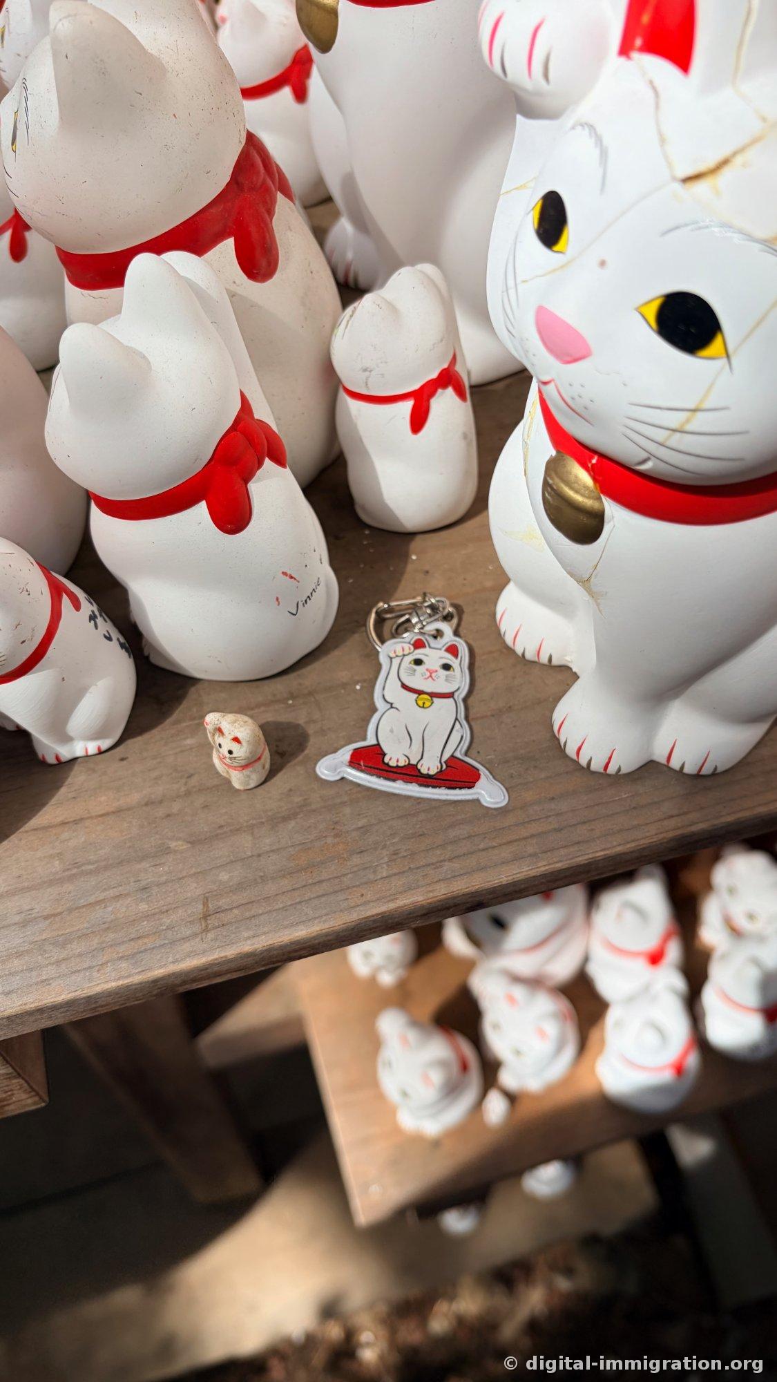 A large cat figurine with golden crackle glaze next to a smaller cat and a beckoning cat keychain