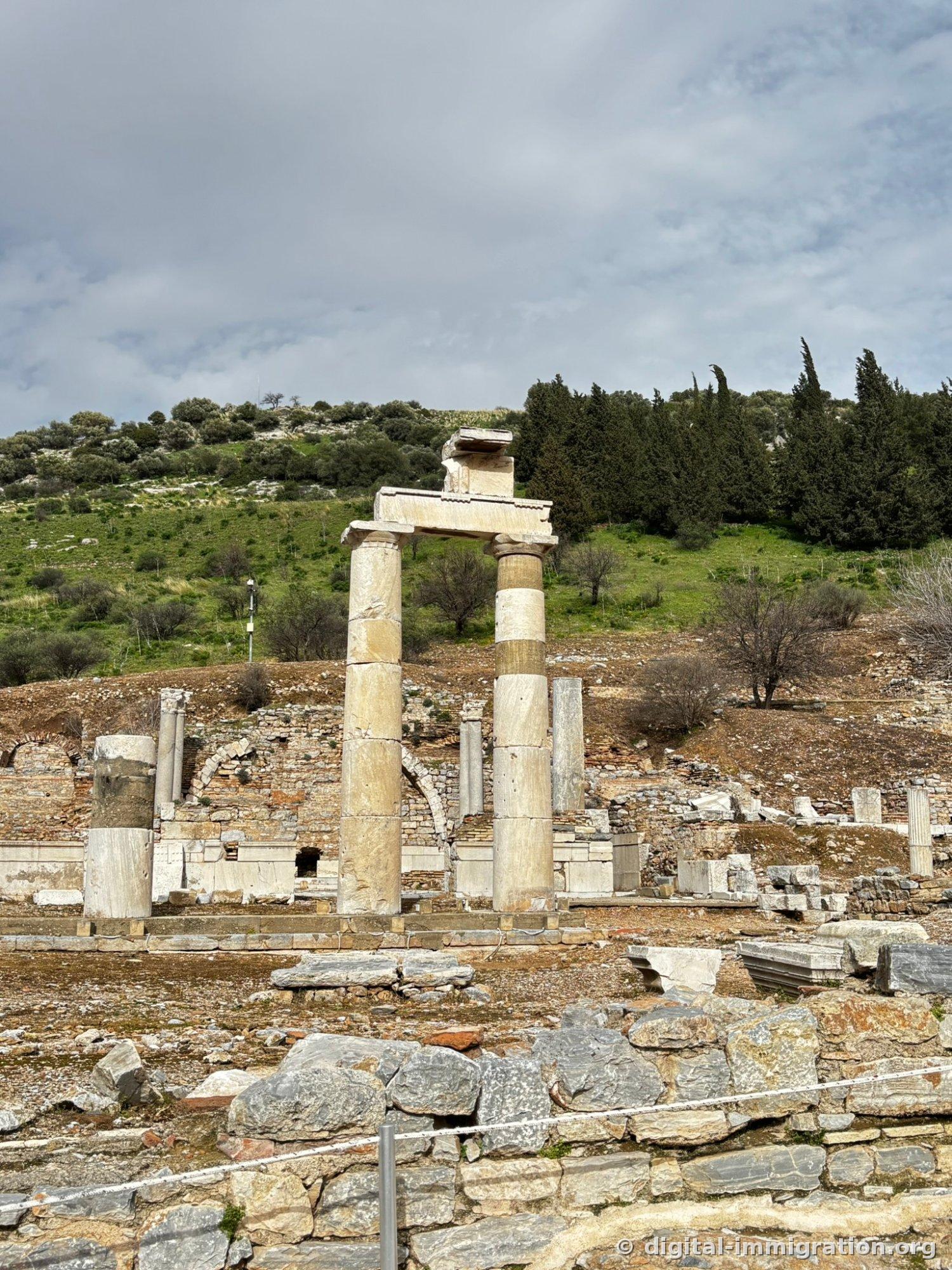 Two cylindrical columns supporting an entablature against a green hillside, a reconstructed structure