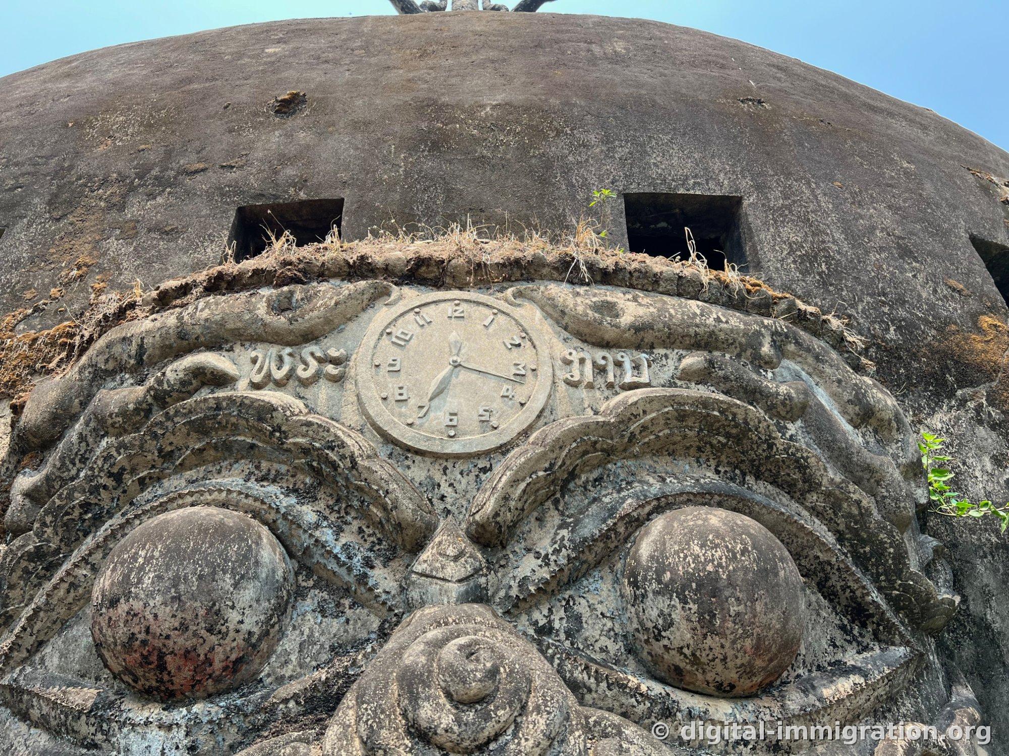 Une horloge en bas-relief gravée au centre du front du visage du démon et des caractères lao, avec de l'herbe sèche poussant au-dessus comme des sourcils