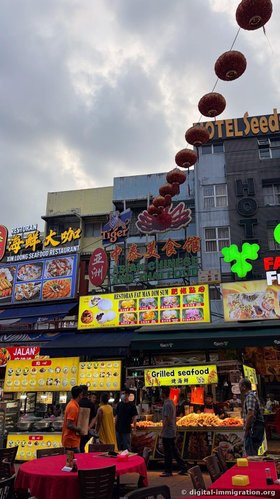 「Xin Loong Seafood Restaurant」「ASIAN CHINESE AND THAI FOOD」「RESTORAN FAT MAN DIM SUM」の看板とその下の点心の陳列台、「Grilled seafood」（焼き海鮮）の屋台が並んだジャランアロール通り