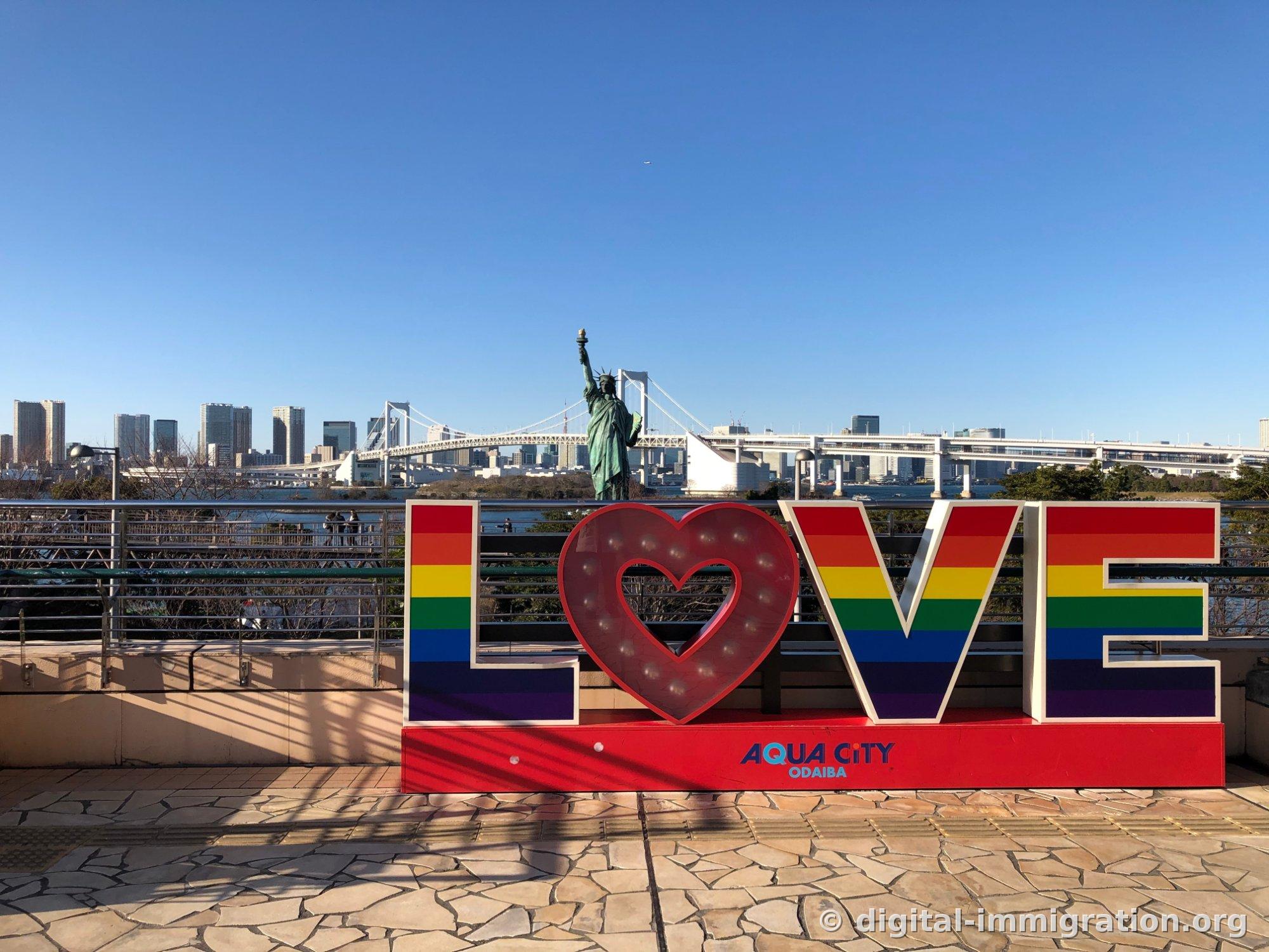 AquaCity台场甲板的彩虹色LOVE装置，背后是自由女神像和彩虹大桥，以及东京市中心高楼