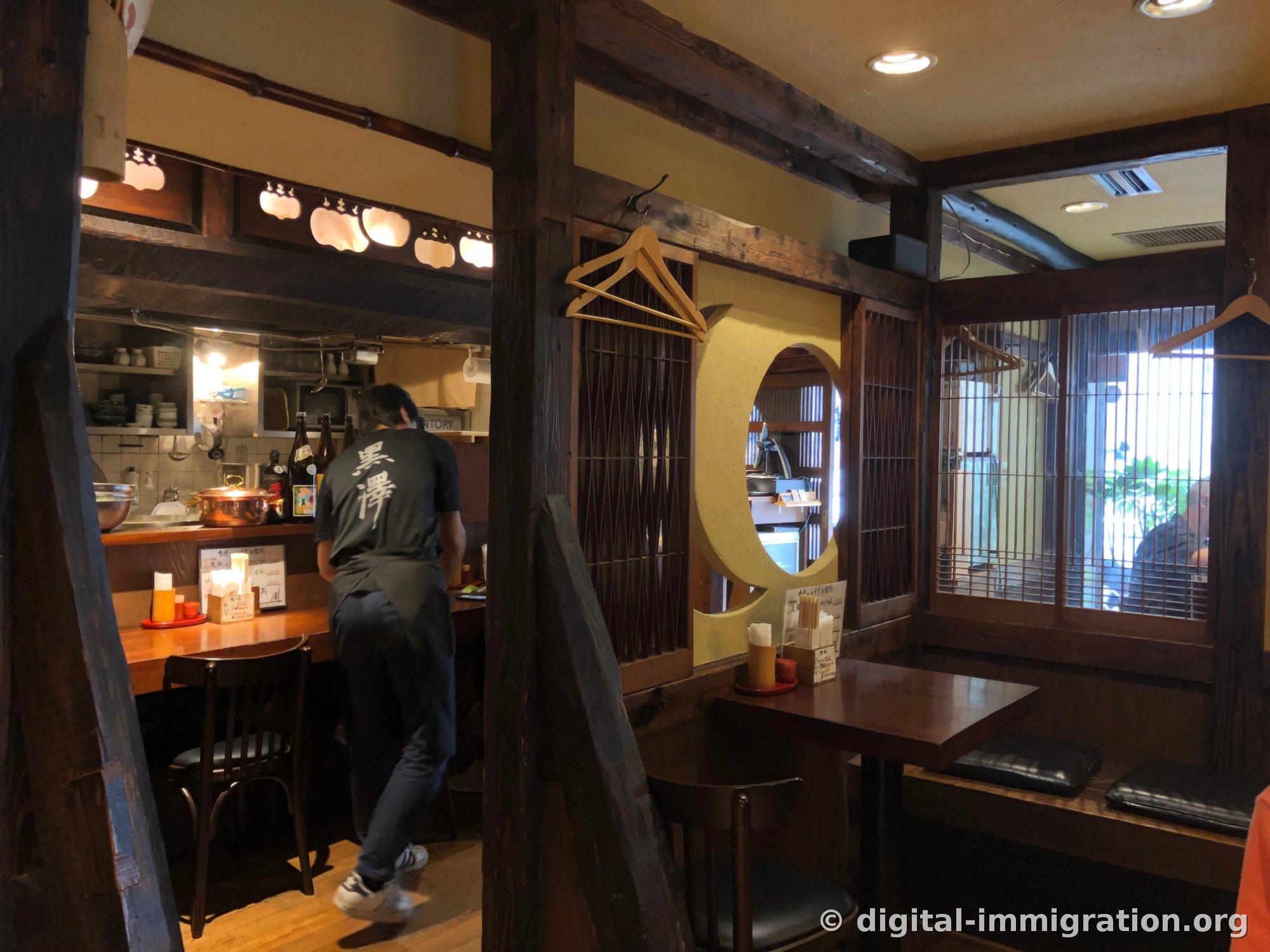 太い木の柱と梁がむき出しのうどん屋の店内。背中に黒澤と書かれたTシャツを着たスタッフがカウンター方向に歩いている