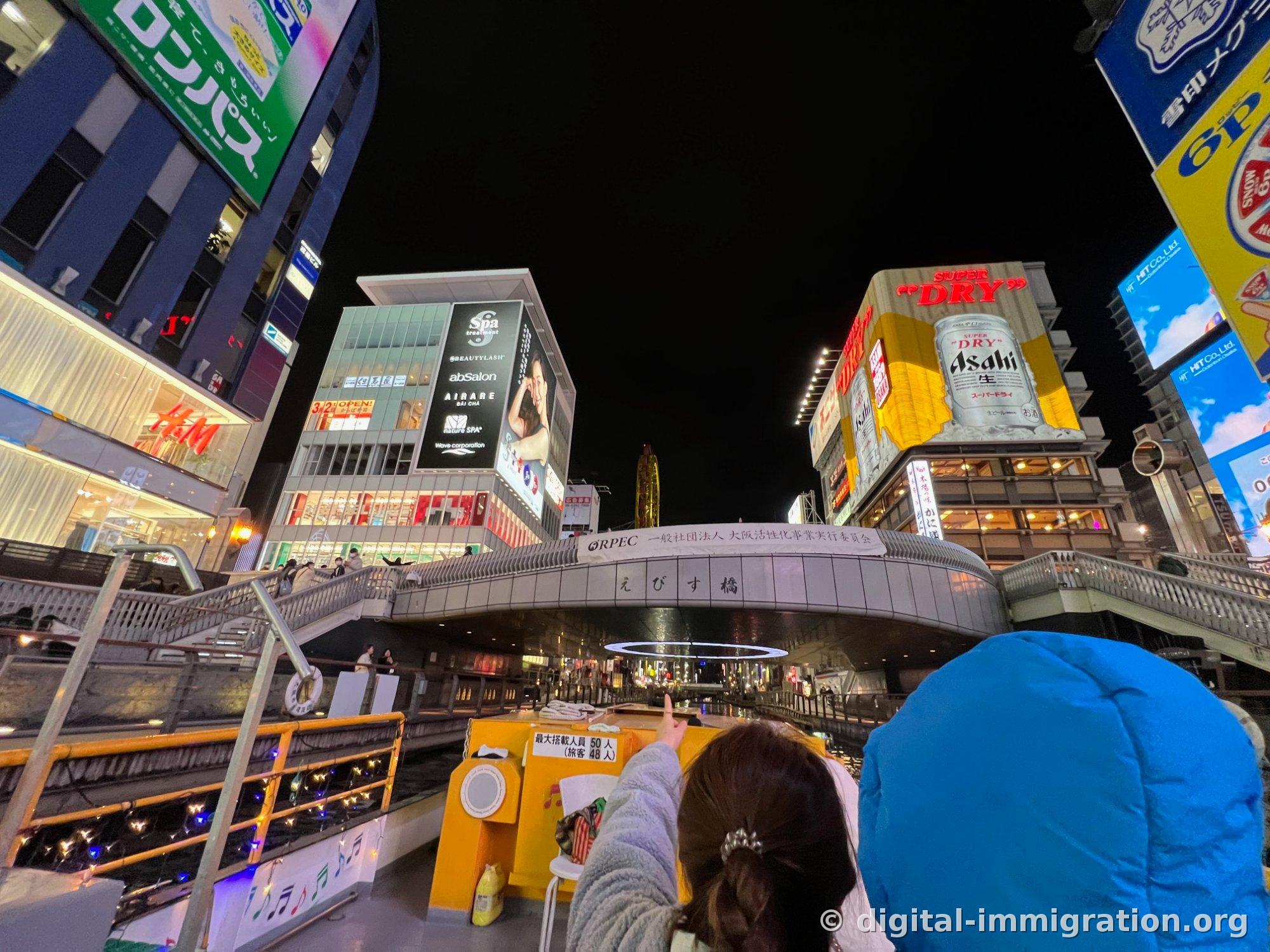 Vue nocturne de l'enseigne Asahi Super Dry et de l'enseigne 6P Cheese visibles côte à côte depuis l'escalier Ebisu