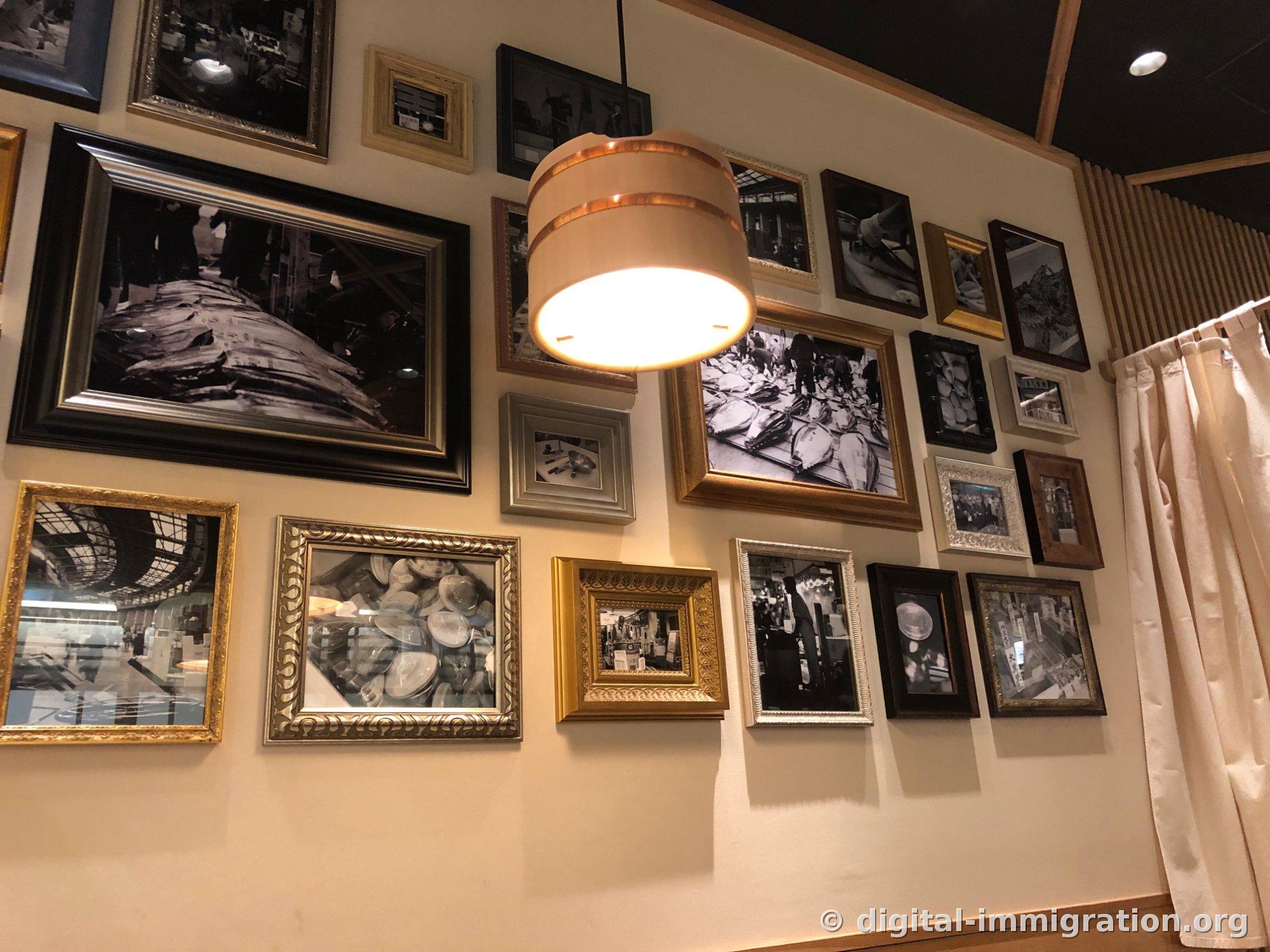 Cadres de photos en noir et blanc de l'ancien marché Tsukiji couvrant un mur du restaurant, avec un abat-jour en forme de bac à riz pour sushis en bois