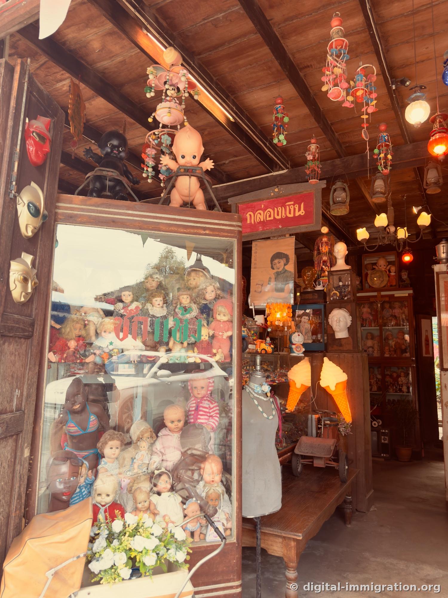 Interior of vintage doll shop with hundreds of dolls in glass cases and hanging mobile, masks, and ice-cream-cone shaped light