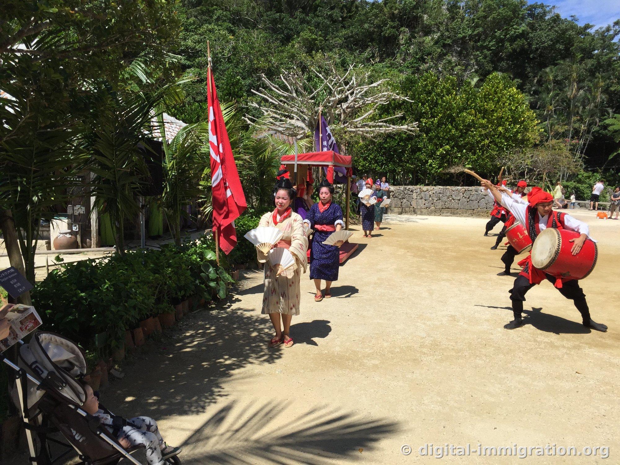 Deux danseuses en tête avec des éventails, suivies de la procession du palanquin, tandis que les musiciens Eisa à droite lèvent leurs baguettes de tambour