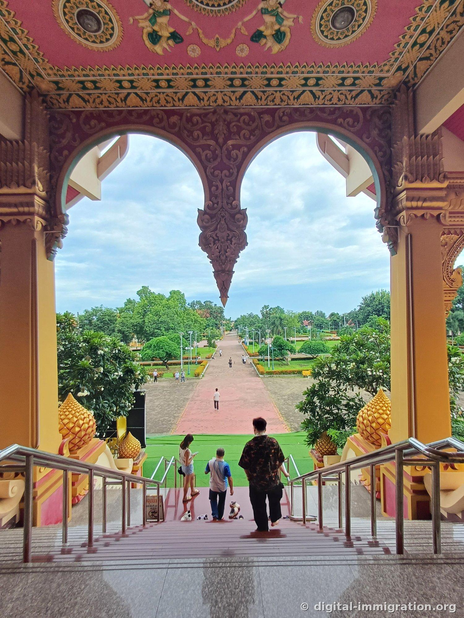 Red pilgrimage path and grounds viewed through carved wooden arches at the temple entrance, people descending steps barefoot
