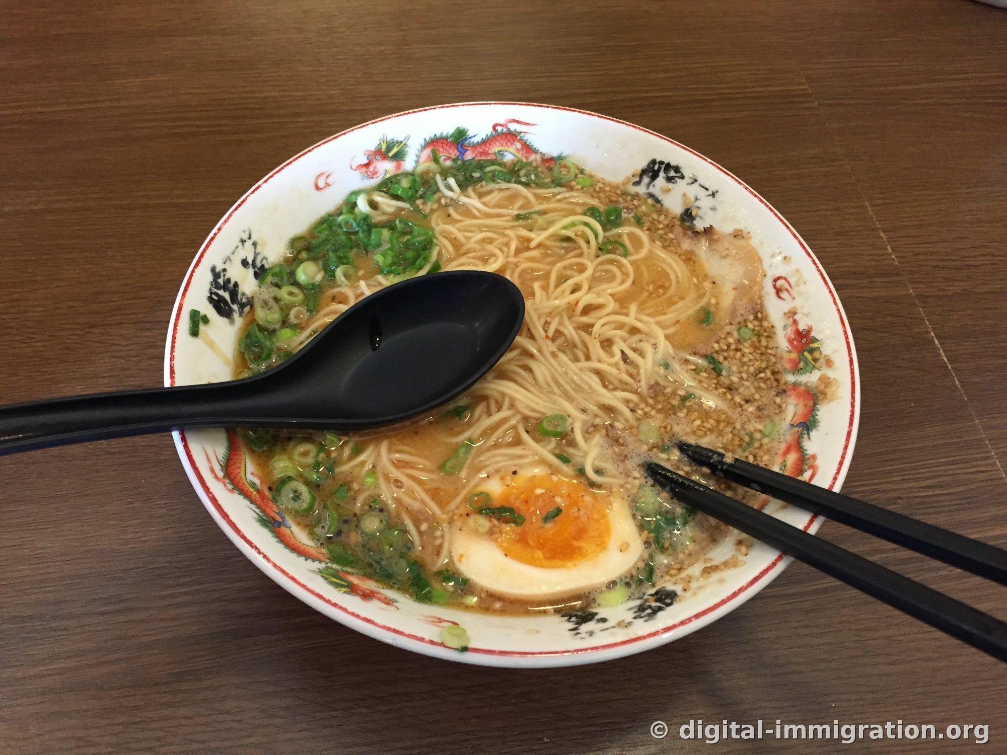 Ramen Negigoma généreusement garni de graines de sésame. Oignons verts, nouilles fines, demi-œuf mollet visible, cuillère ramen noire posée sur le bol