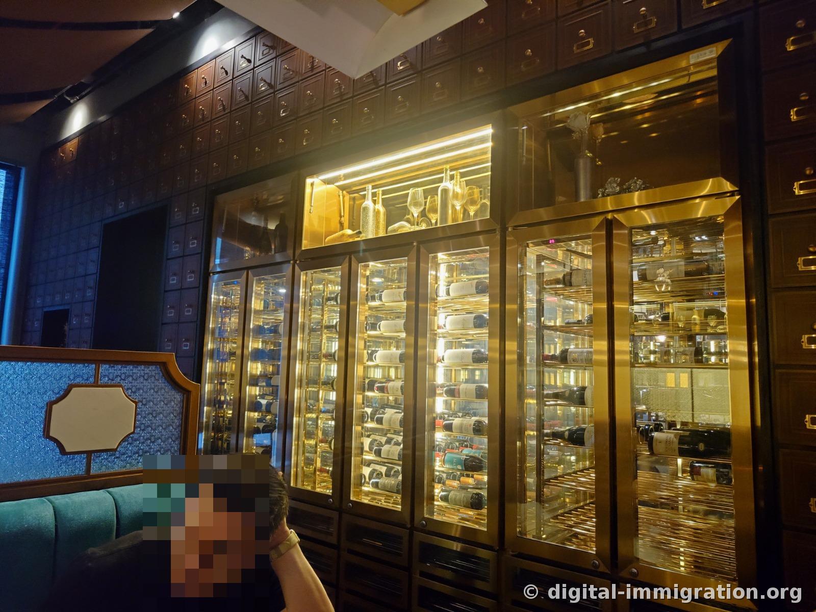 Illuminated wine cellar with wine bottles stored horizontally inside brass-framed glass doors and wooden drawer cabinet wall