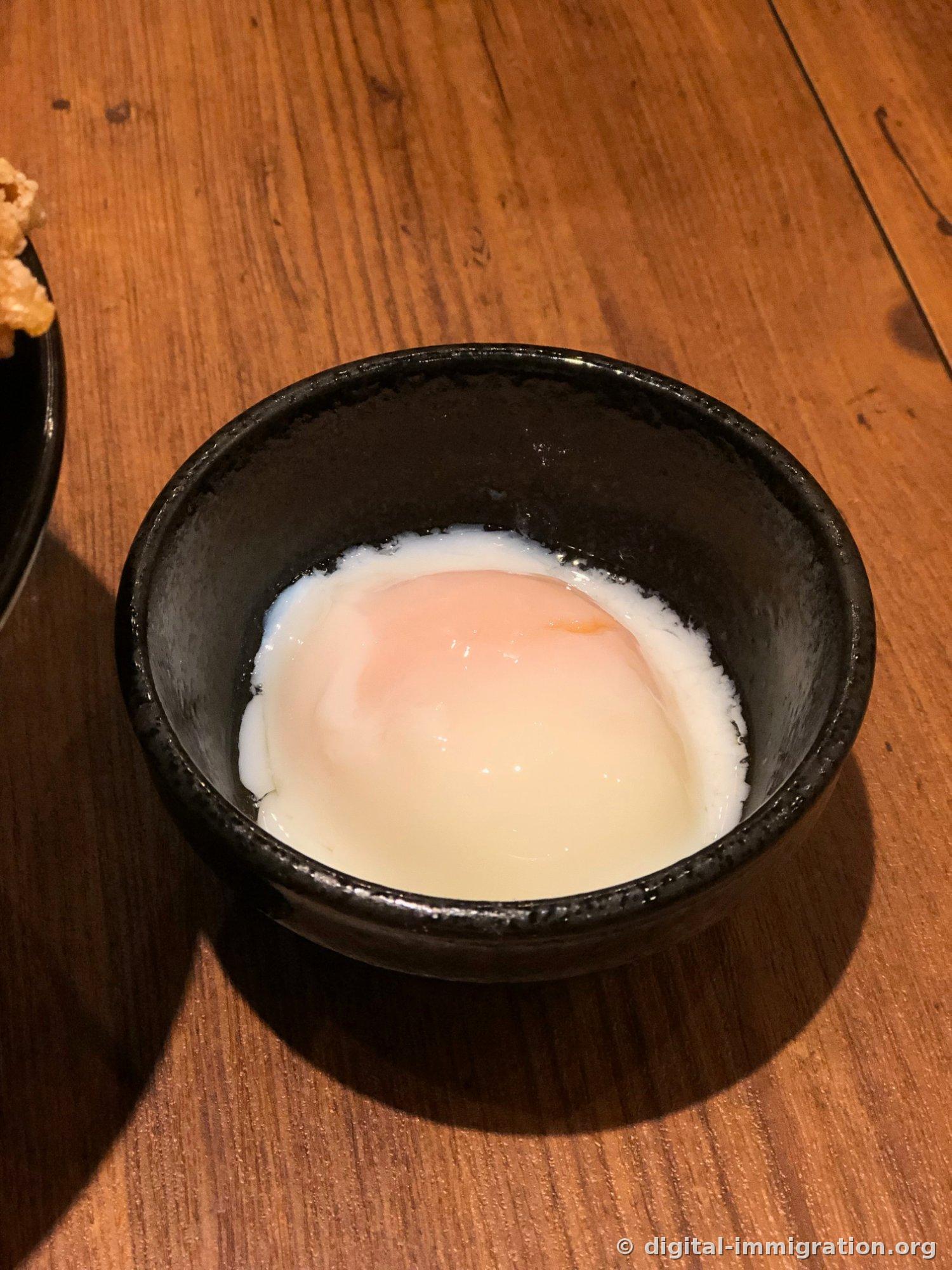 Un petit bol noir sur une table en bois contenant un œuf mollet source chaude, avec le blanc durci et le jaune coulant